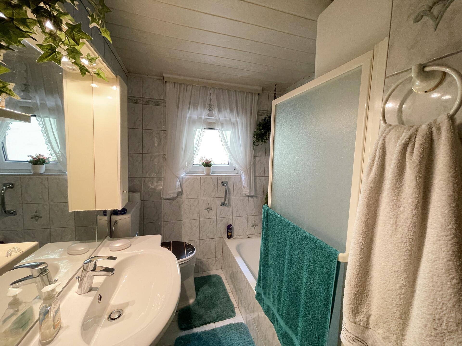 Badezimmer mit Badewanne, Duschabtrennung und Fenster für Tageslicht.