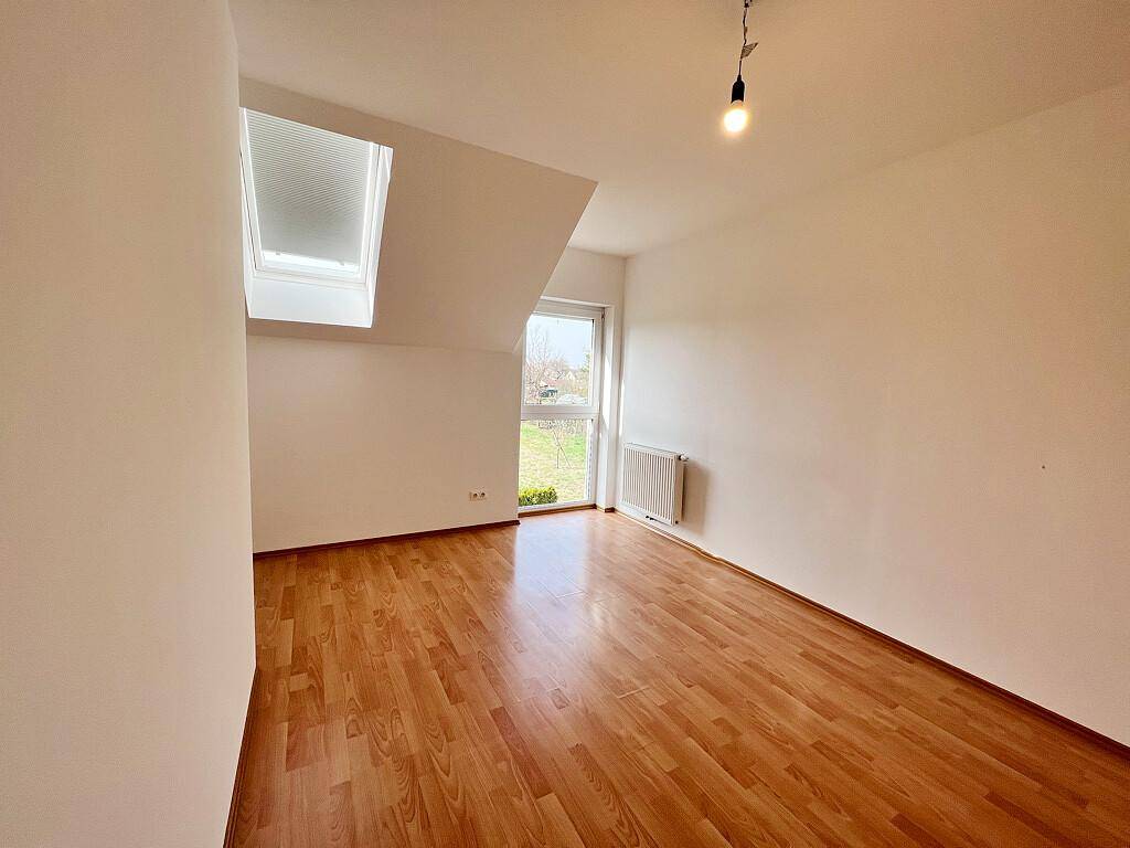Freundliches Schlafzimmer mit Laminatboden, Dachschräge und Fenster mit Jalousie.