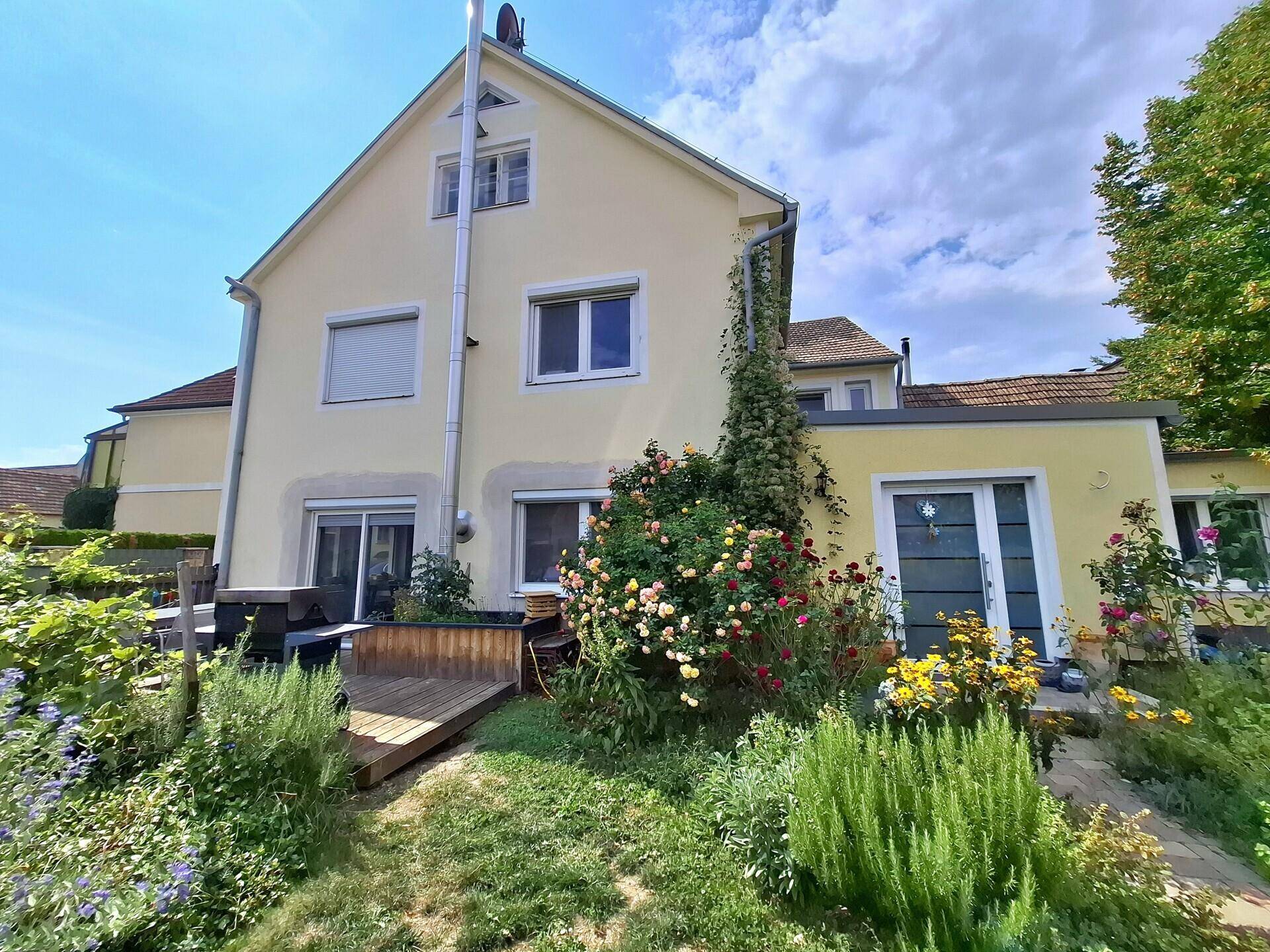 Rückansicht des Hauses mit Terrasse, blühenden Rosen und einem gepflegten Garten.