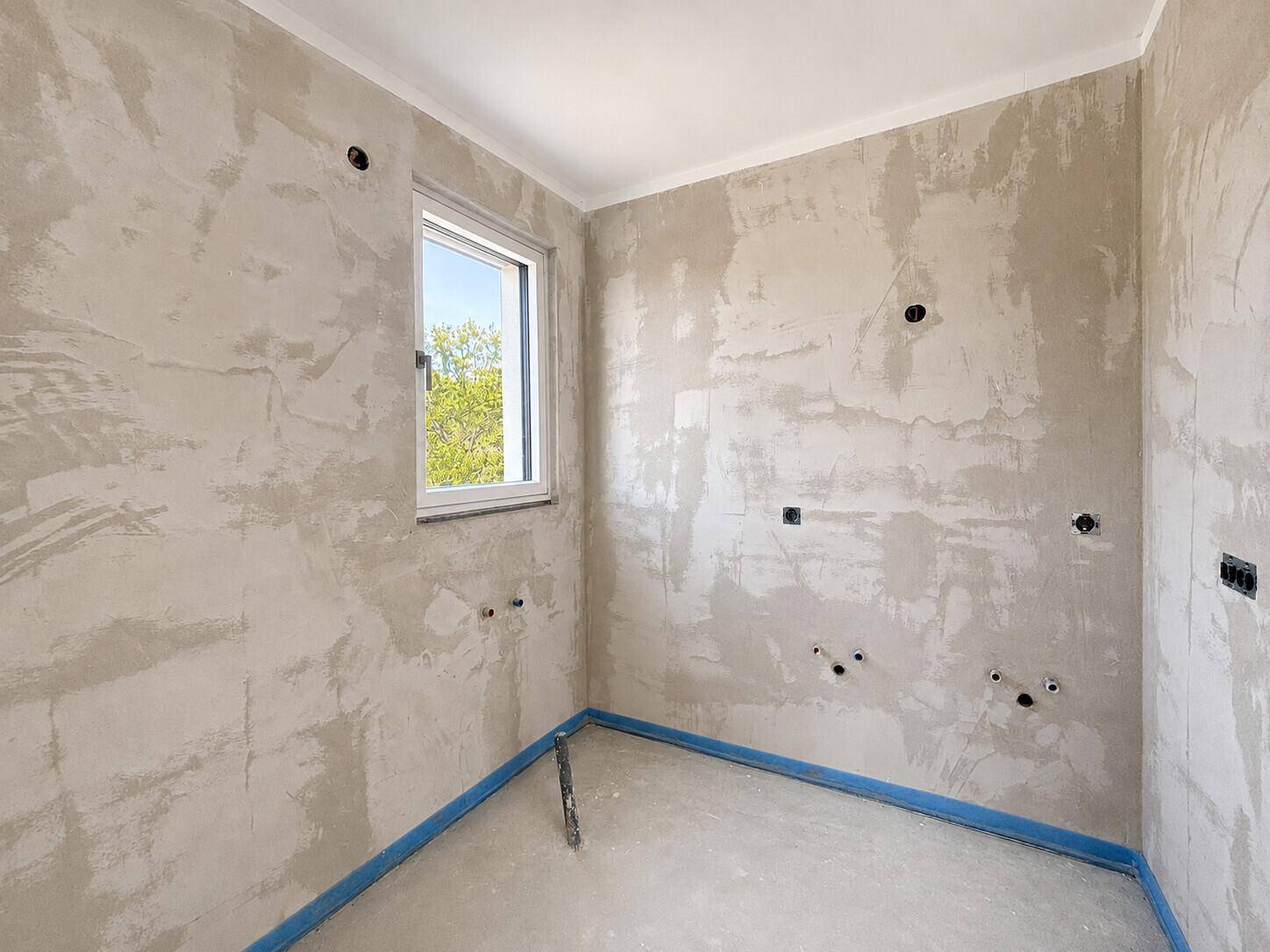 Unfertiger Raum mit Fenster und vorbereiteten Anschlüssen, ideal als Hauswirtschaftsraum oder kleines Bad.