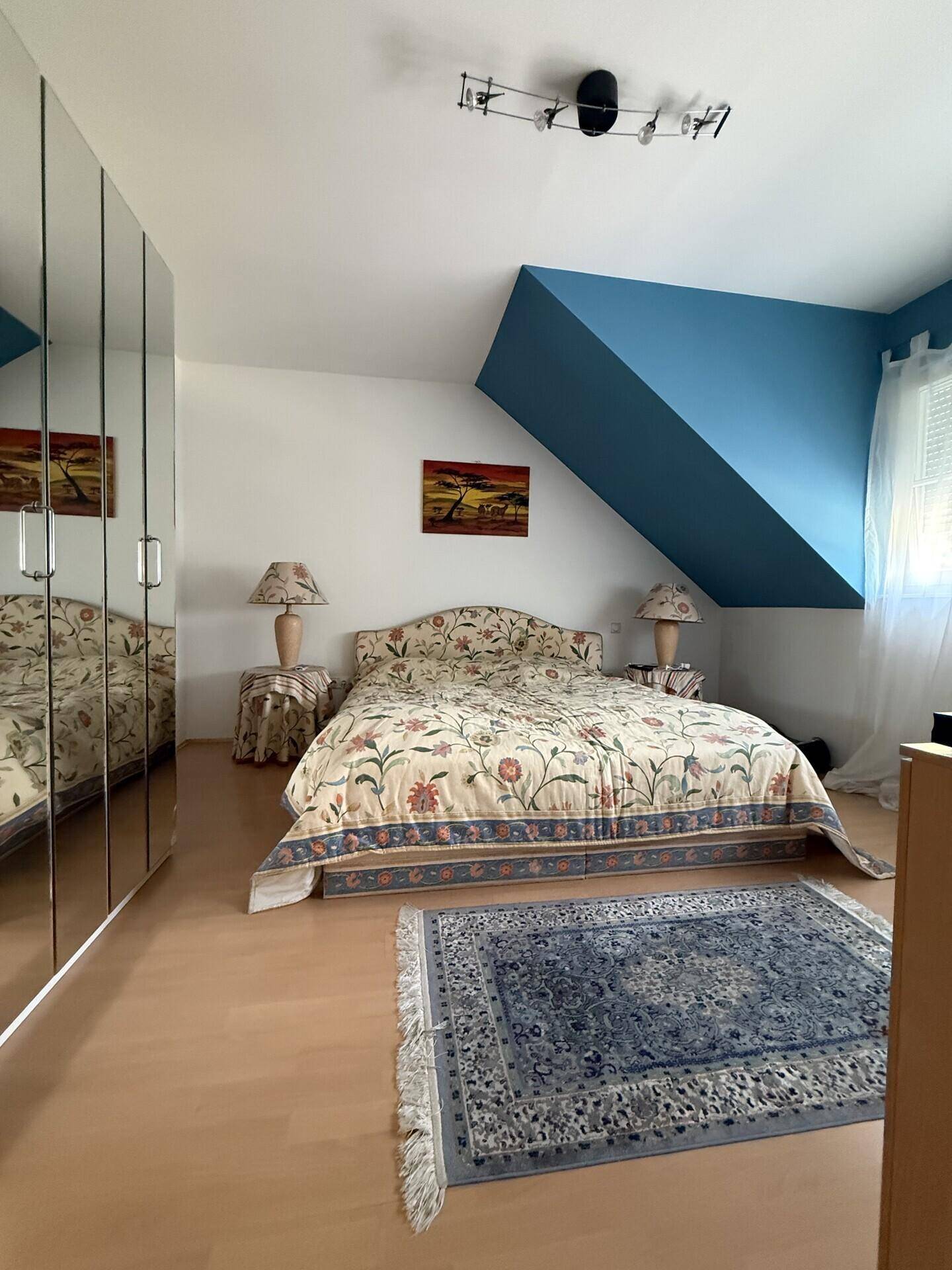 Helles Schlafzimmer mit floraler Bettwäsche, Spiegelschränken und Dachschräge.