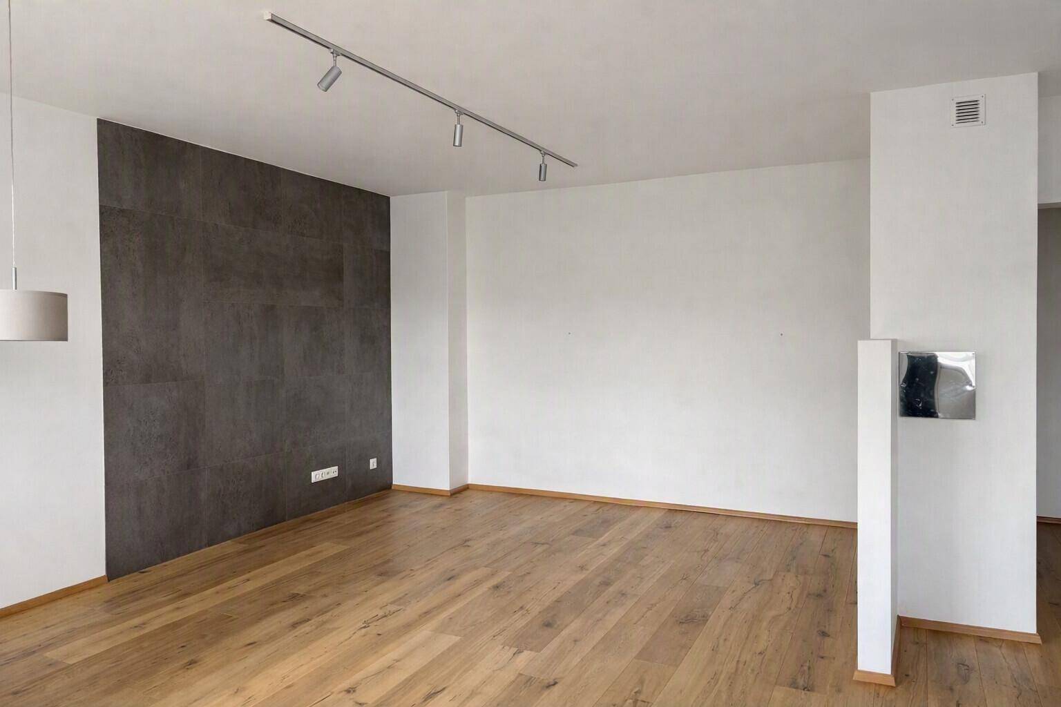 Geräumiges Wohnzimmer mit Holzboden und einer dunklen Akzentwand, bereit zur individuellen Gestaltung.