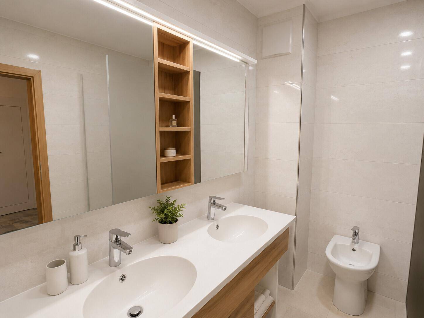 Modernes Badezimmer mit Doppelwaschbecken, großem Spiegel, Bidet und hellen Fliesen.