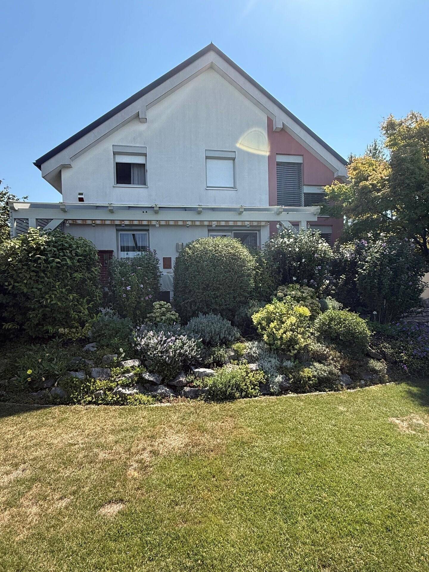 Rückansicht des Hauses mit farbenfrohen Blumenbeeten und gepflegter Gartenlandschaft.