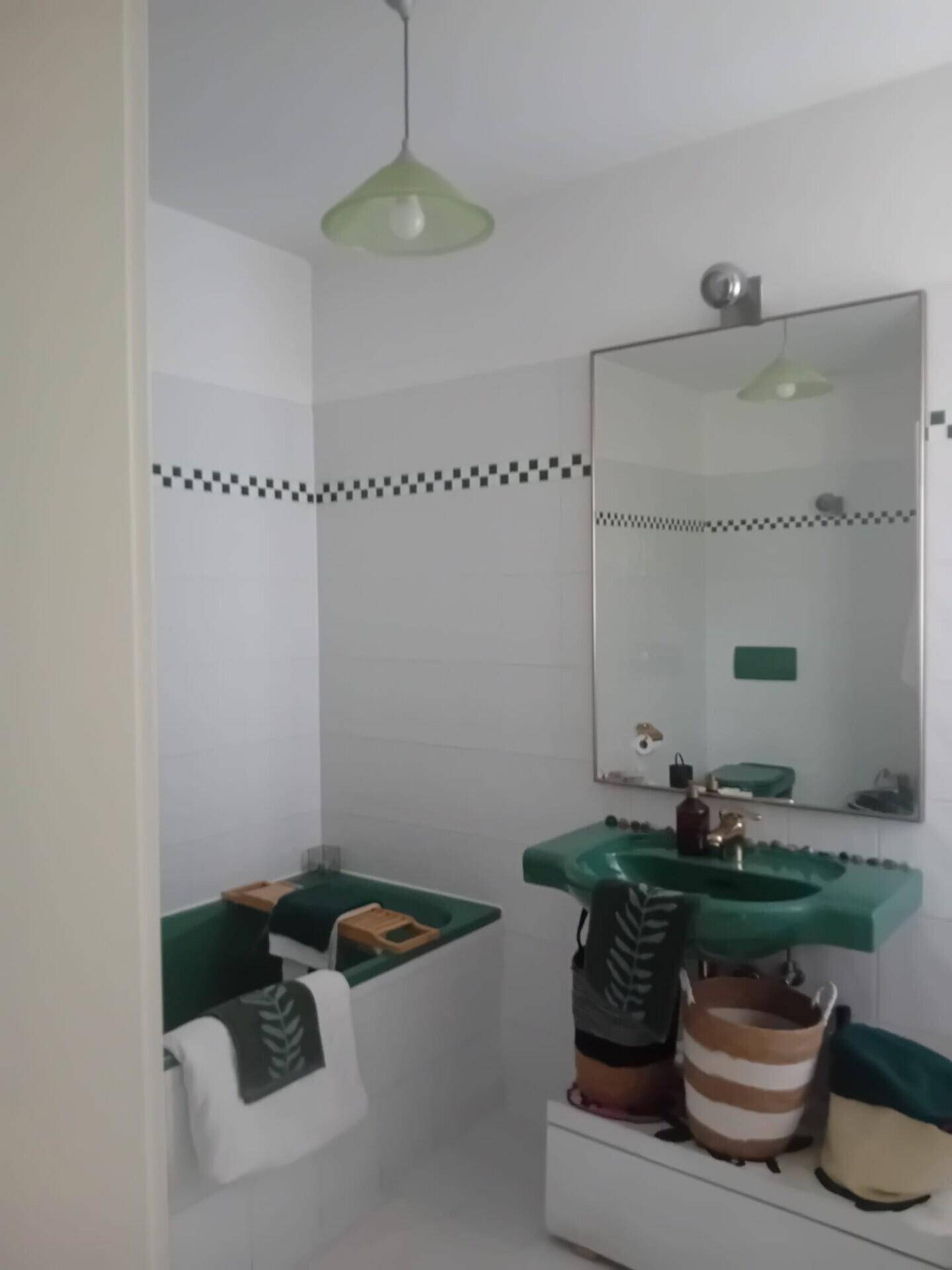 Badezimmer mit grüner Badewanne und Waschbecken, weißen Fliesen und Spiegel.