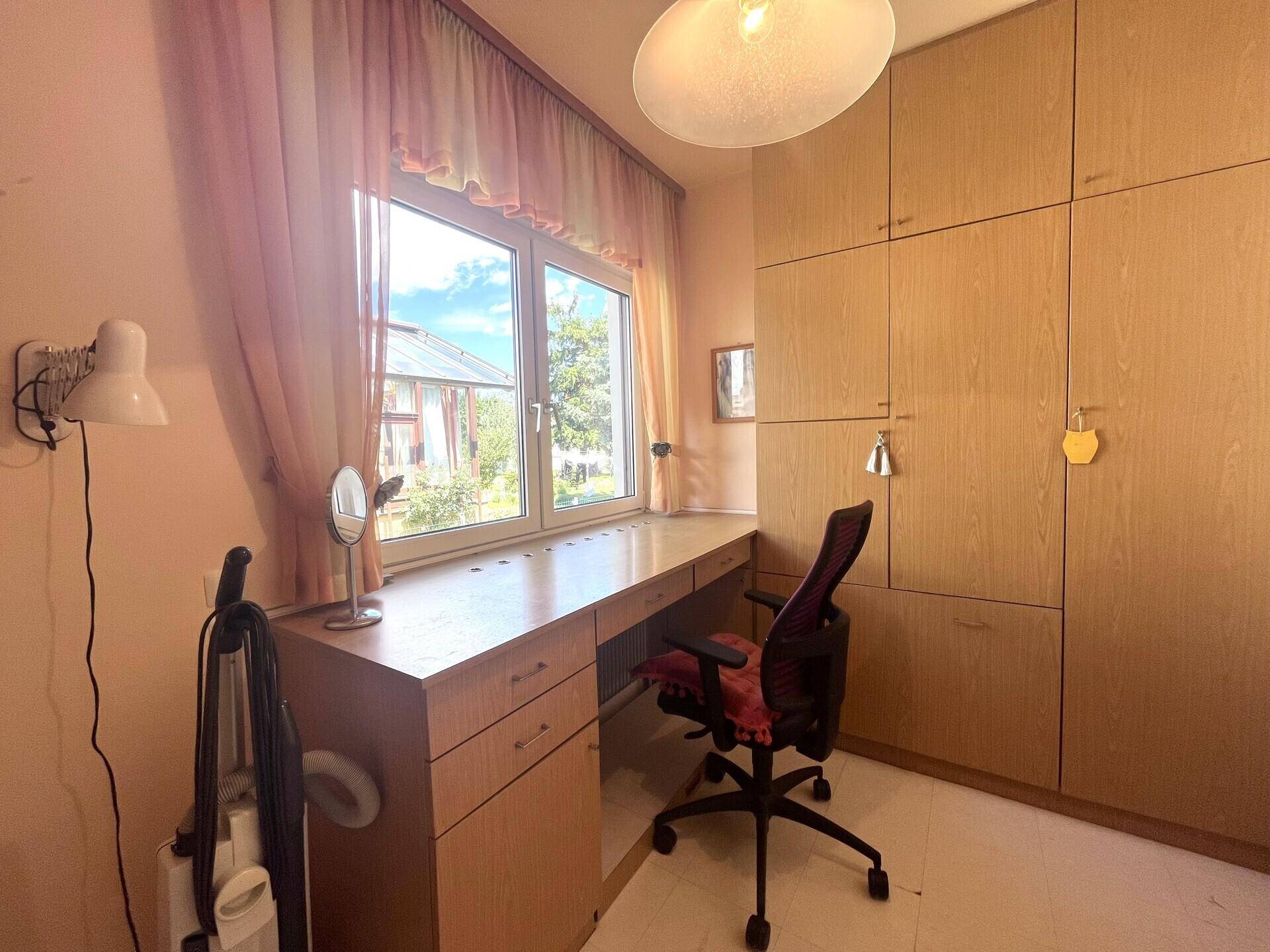 Funktionales Arbeitszimmer mit Schreibtisch, Bürostuhl und eingebauten Holzschränken am Fenster.