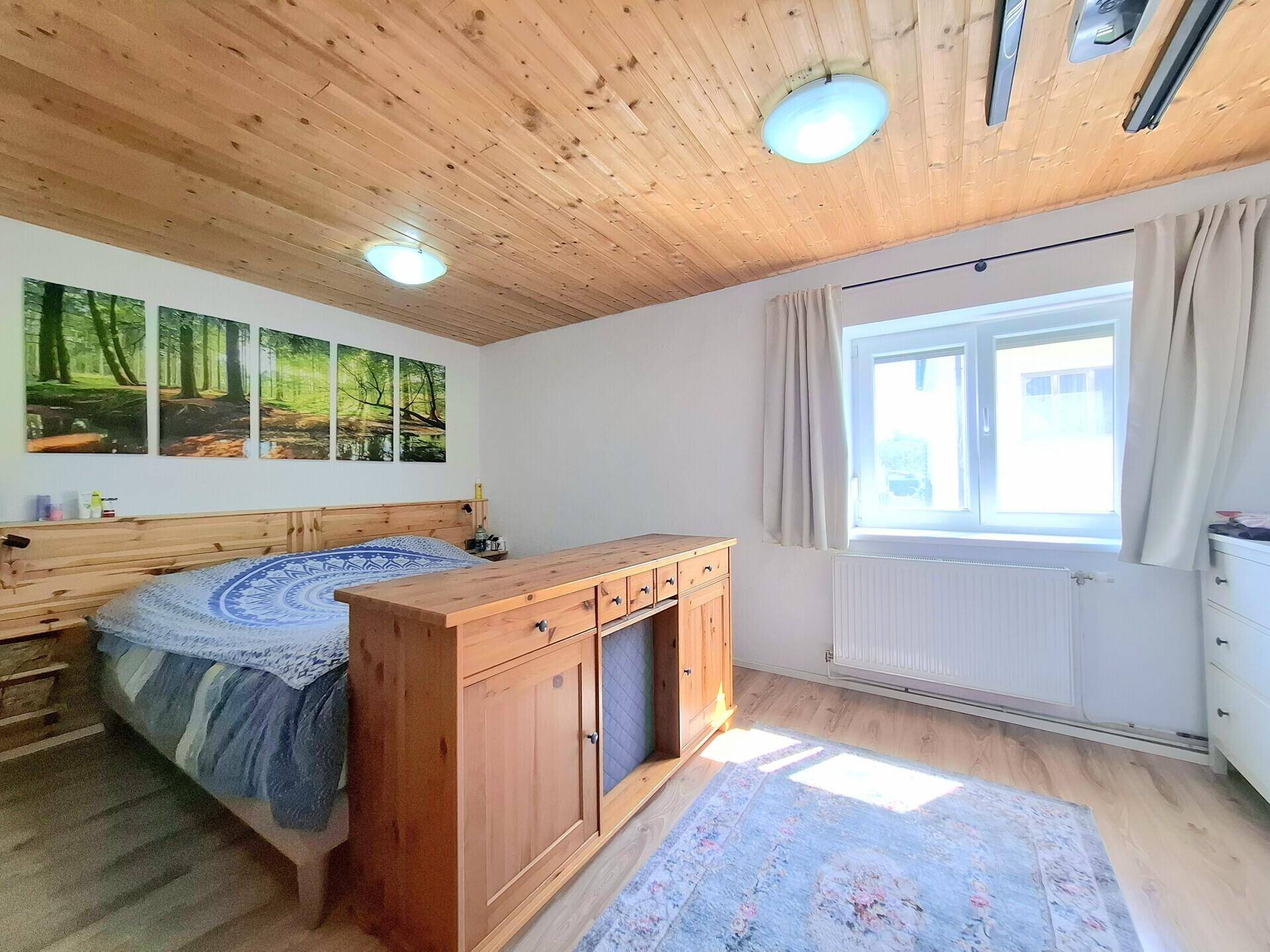 Gemütliches Schlafzimmer mit Holzbalkendecke, Doppelbett und Teppich auf Laminatboden.