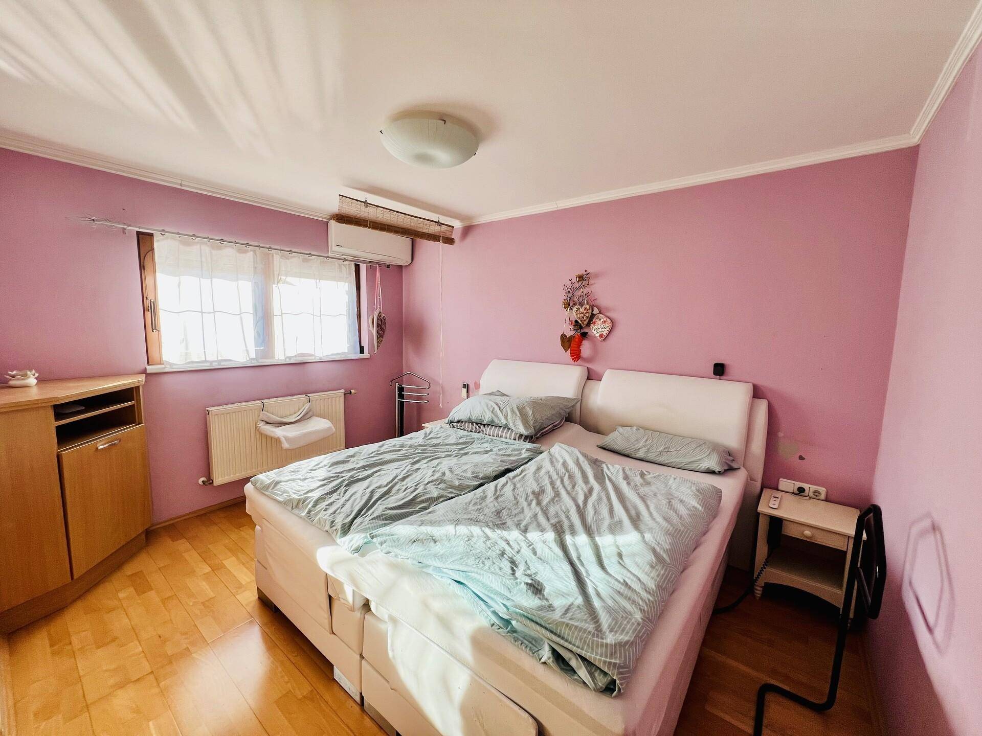 Schlafzimmer mit Doppelbett, rosa Wänden, Holzboden und Klimaanlage.