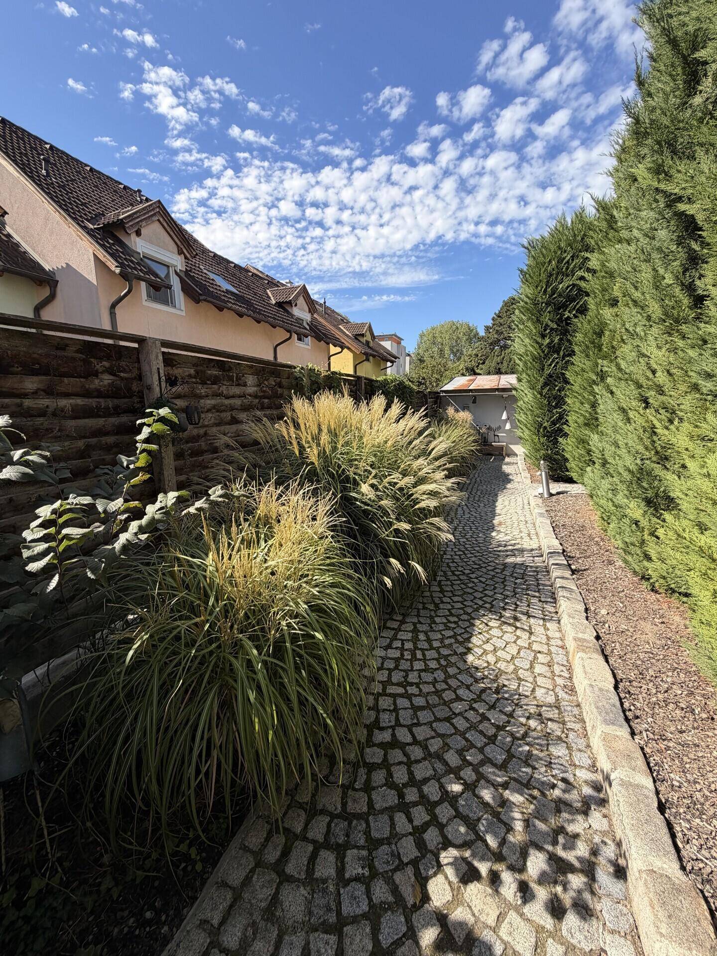 Geschwungener Gartenweg aus Kopfsteinpflaster, umgeben von üppiger Bepflanzung.
