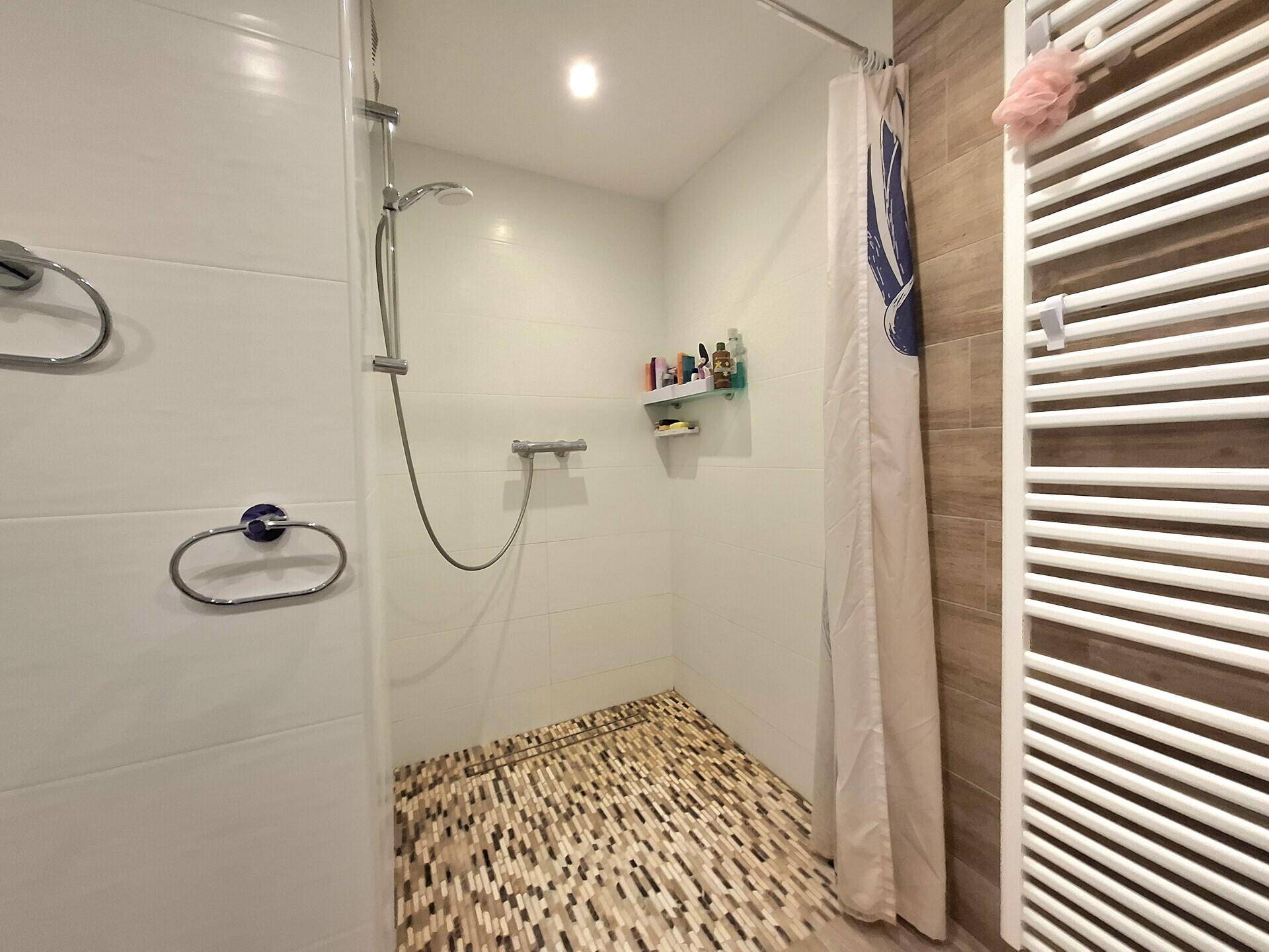 Moderne Duschkabine mit Mosaikfliesen und weißer Wandverkleidung, ausgestattet mit Handtuchhalter.