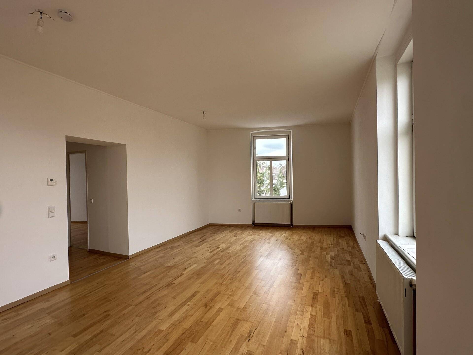 Großzügiges Wohnzimmer mit Parkettboden und mehreren Fenstern, die für viel Tageslicht sorgen.