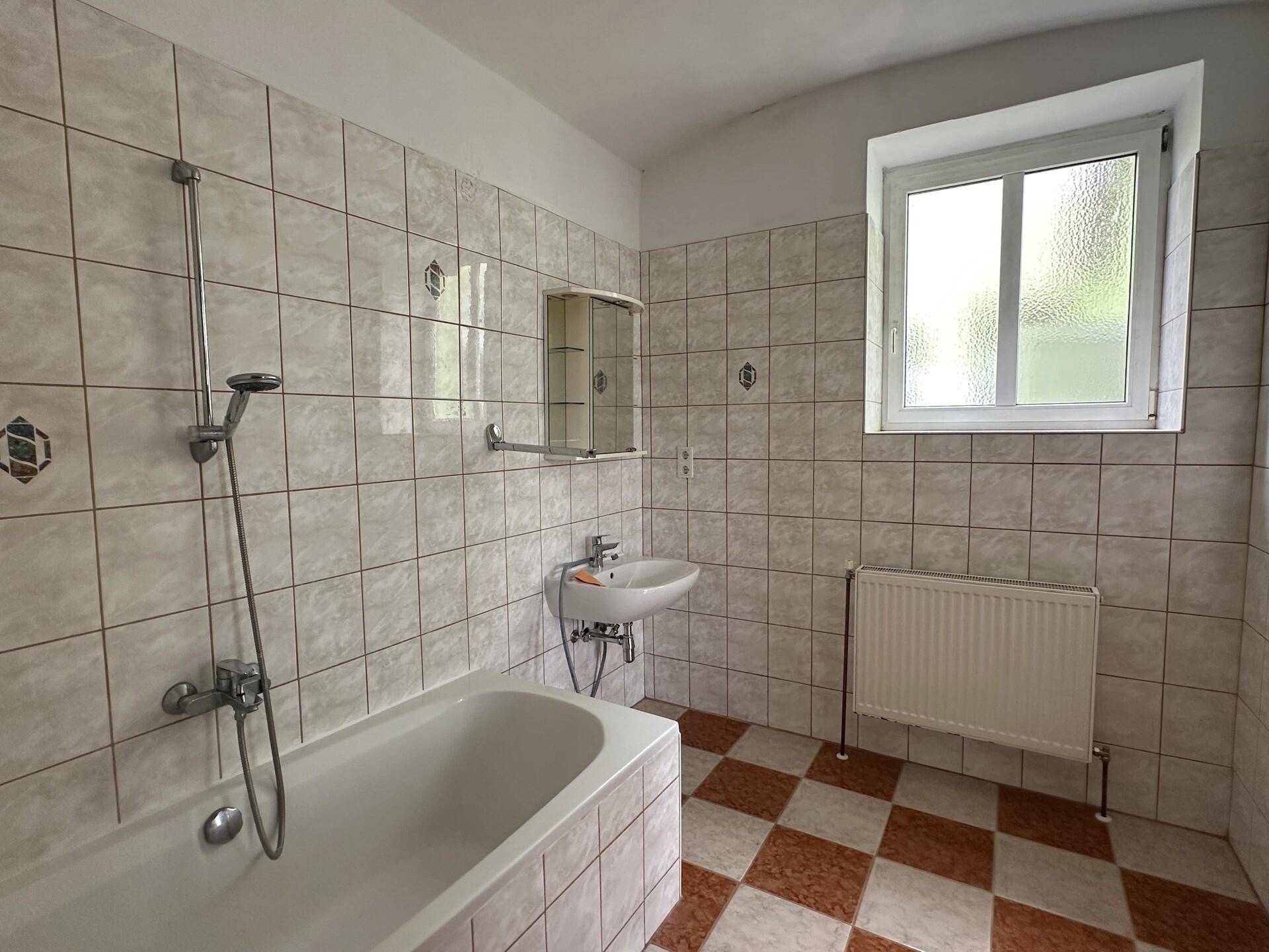 Badezimmer mit Badewanne, Heizkörper und Fenster für natürliche Belüftung.