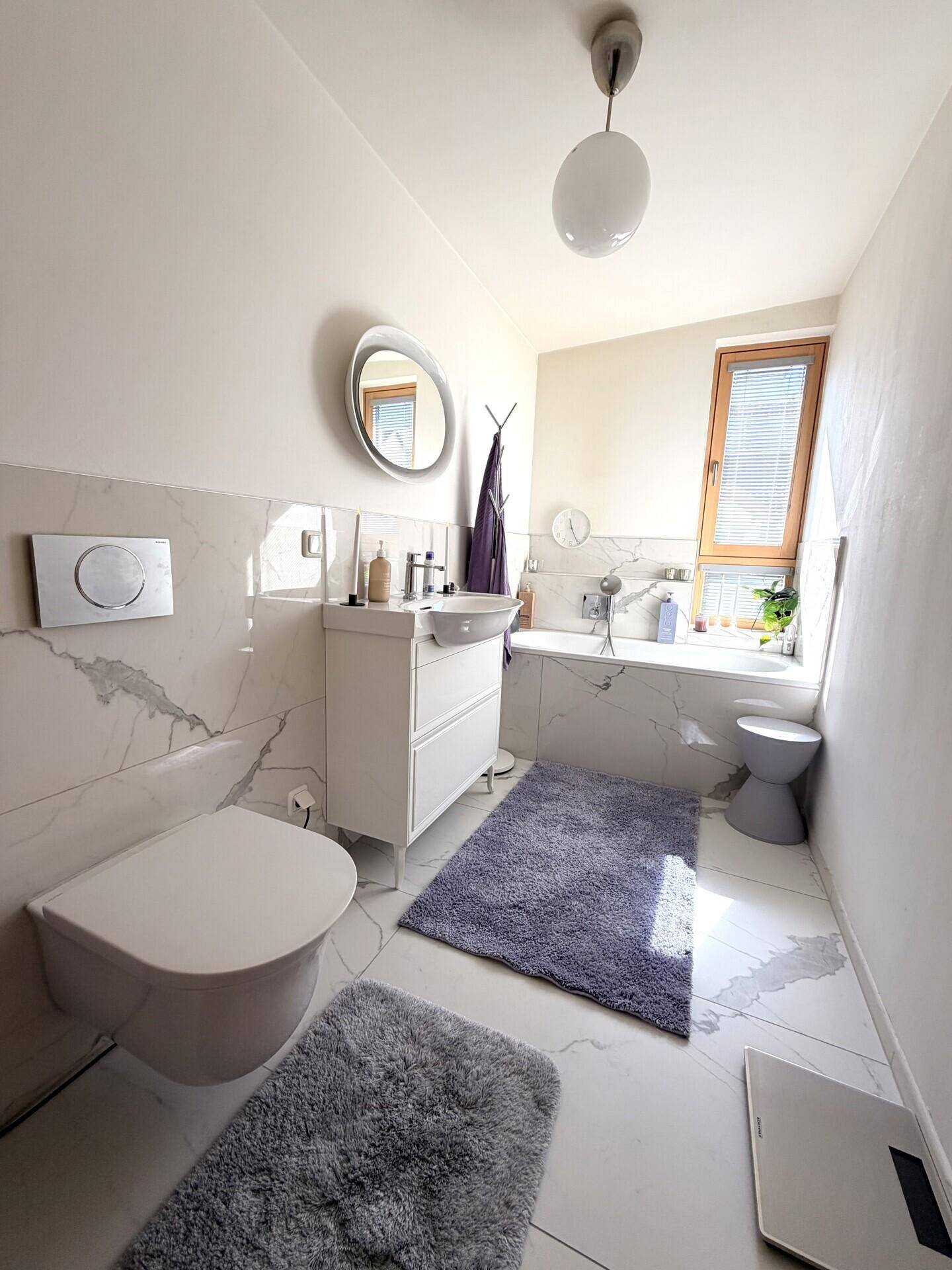 Modernes Badezimmer mit weißen Marmorfliesen, Badewanne und Fenster.