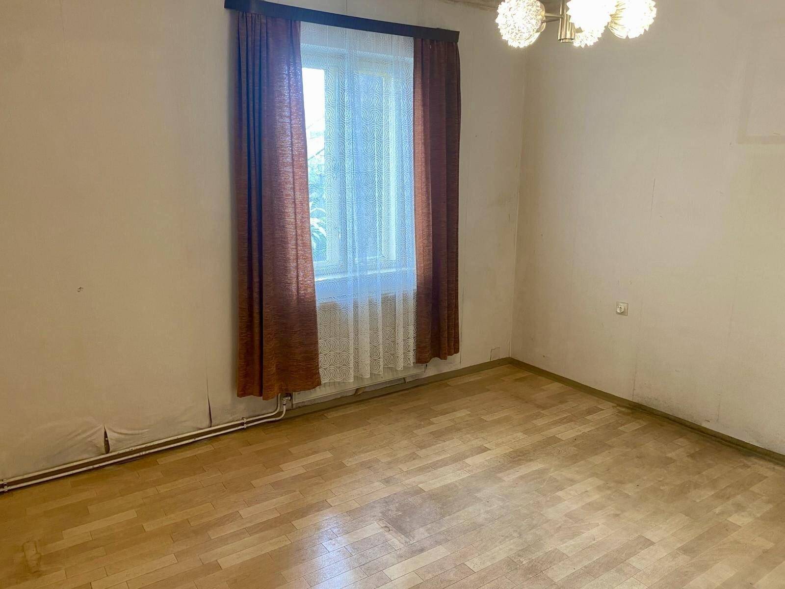 Einfaches Zimmer mit Parkettboden, Fenster und einem Heizkörper unter dem Fenster.