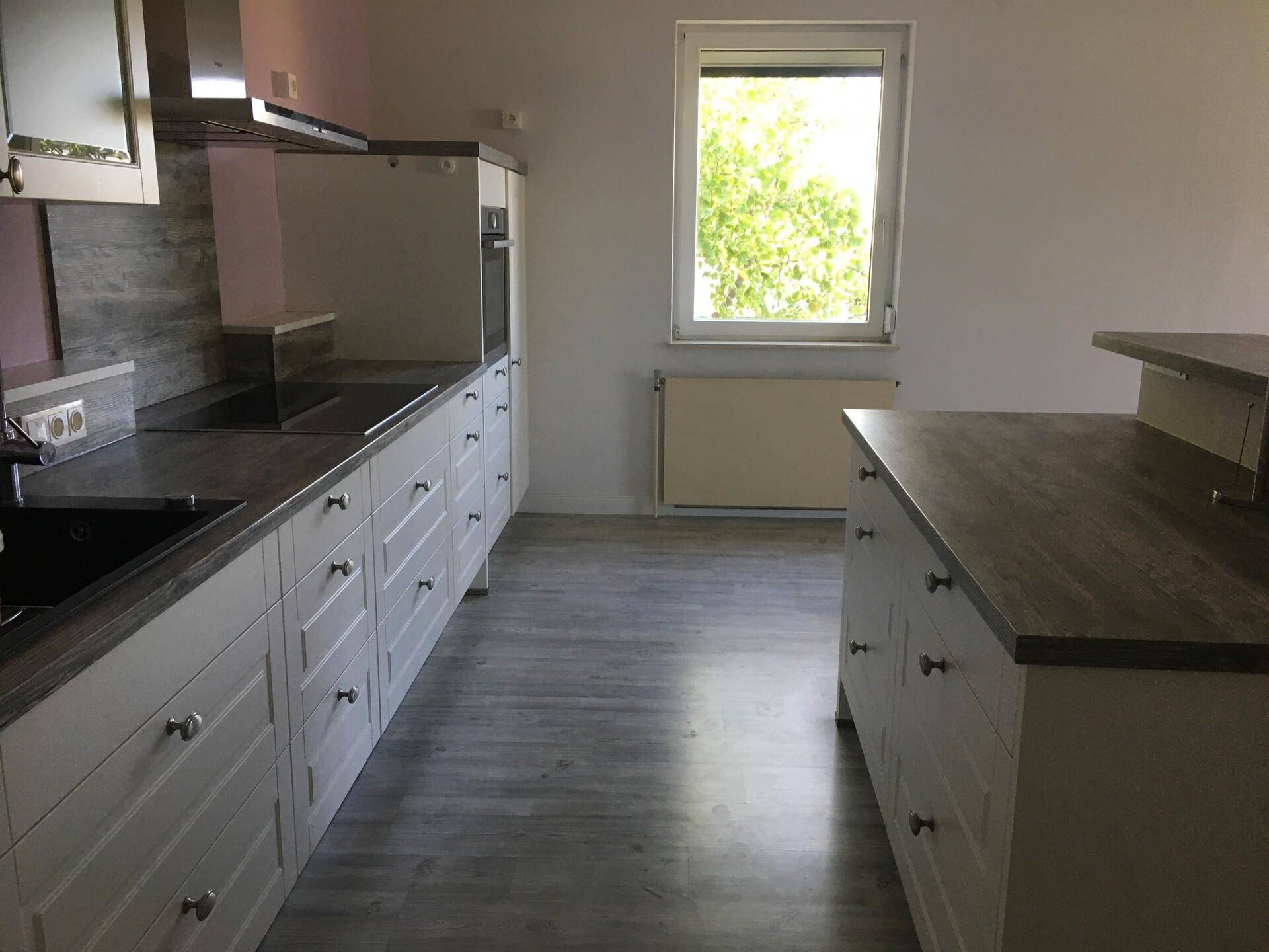 Moderne Küche mit weißen Schränken, dunklen Arbeitsplatten und Laminatboden.