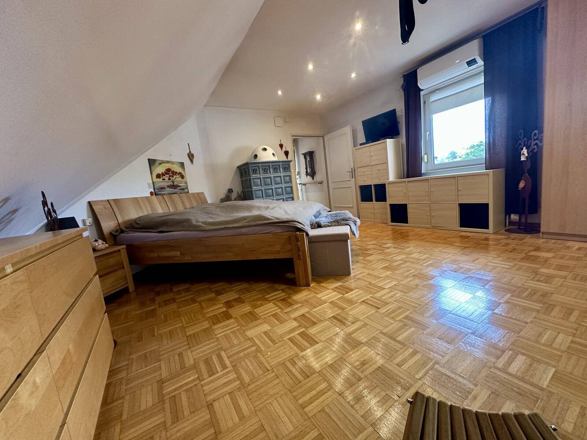Geräumiges Schlafzimmer im Dachgeschoss mit Holzboden, Doppelbett und Kachelofen.