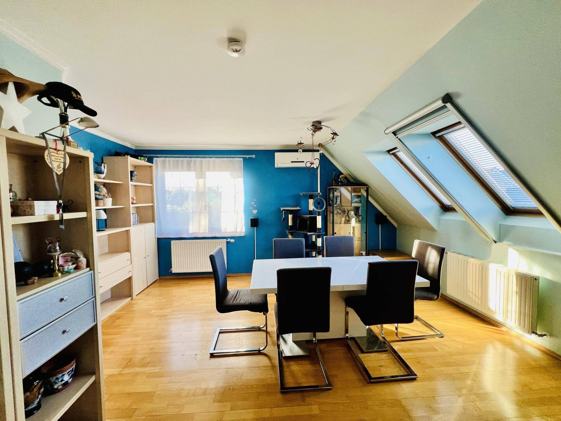 Essbereich im Dachgeschoss mit Holzboden, blauen Wänden und Dachfenstern.