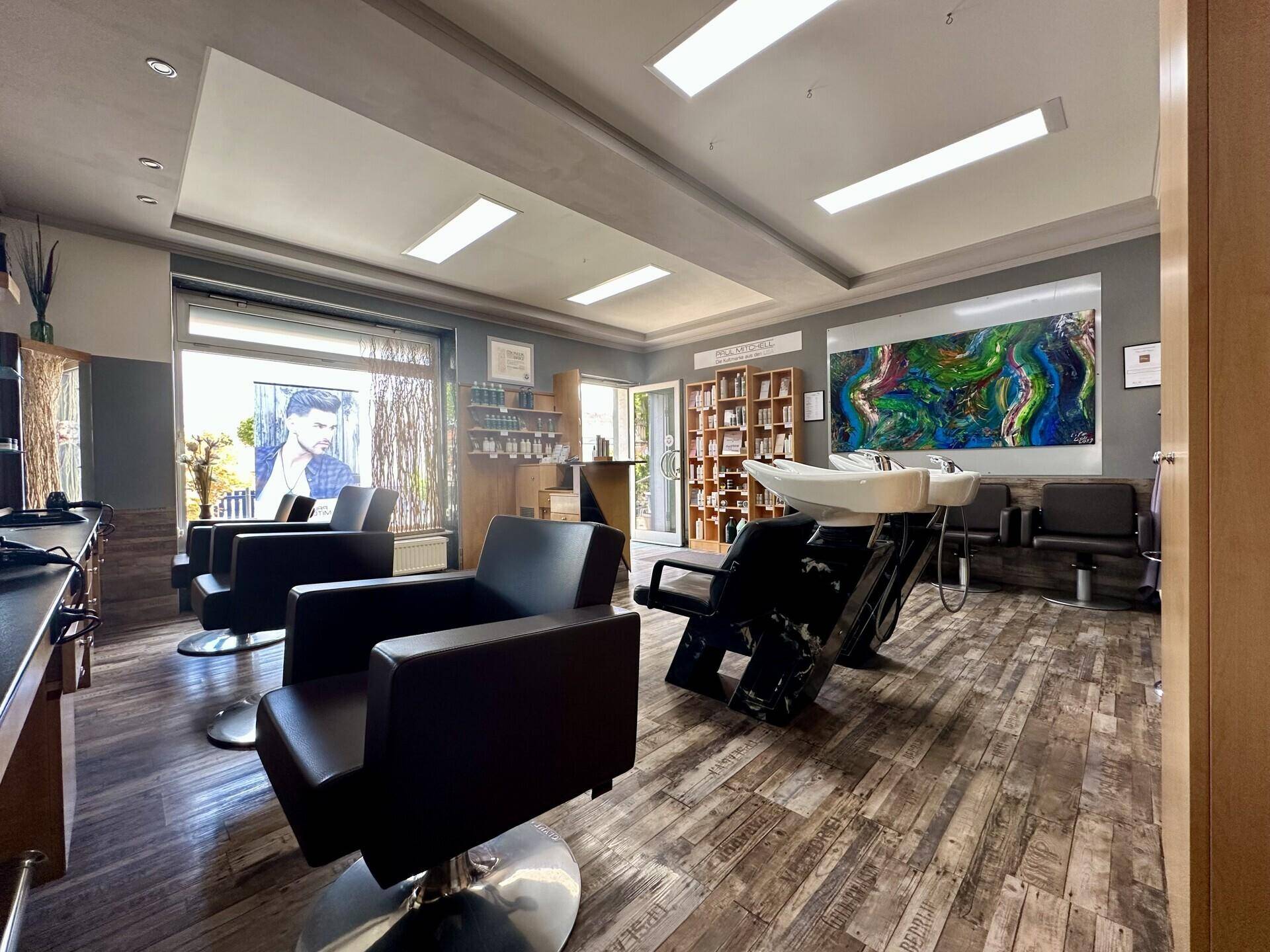 Moderner Friseursalon mit mehreren Styling-Stationen, Waschbecken und Produktregalen, hell beleuchtet.