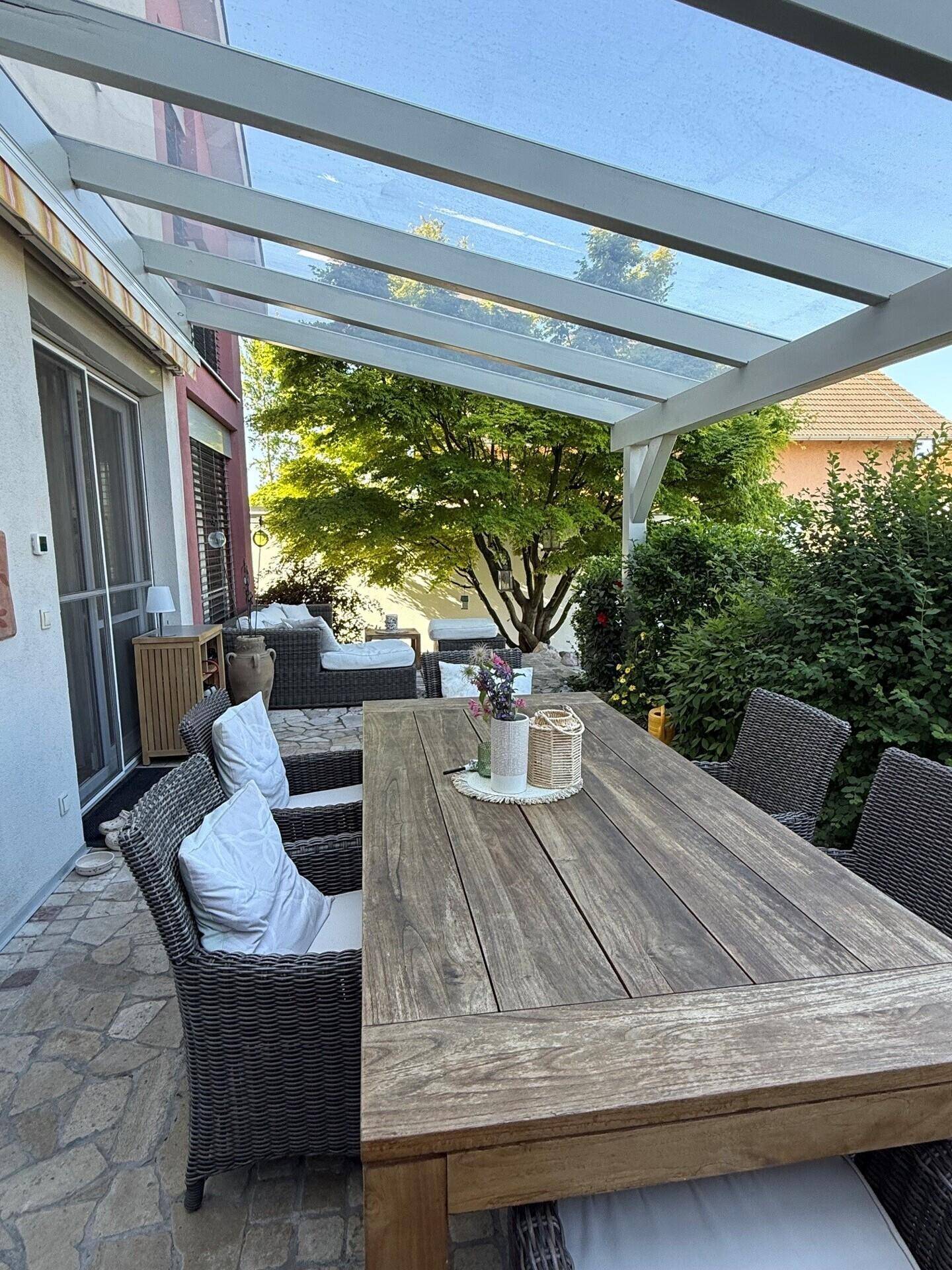 Überdachte Terrasse mit großem Holztisch und Gartenmöbeln, ideal für Mahlzeiten im Freien.