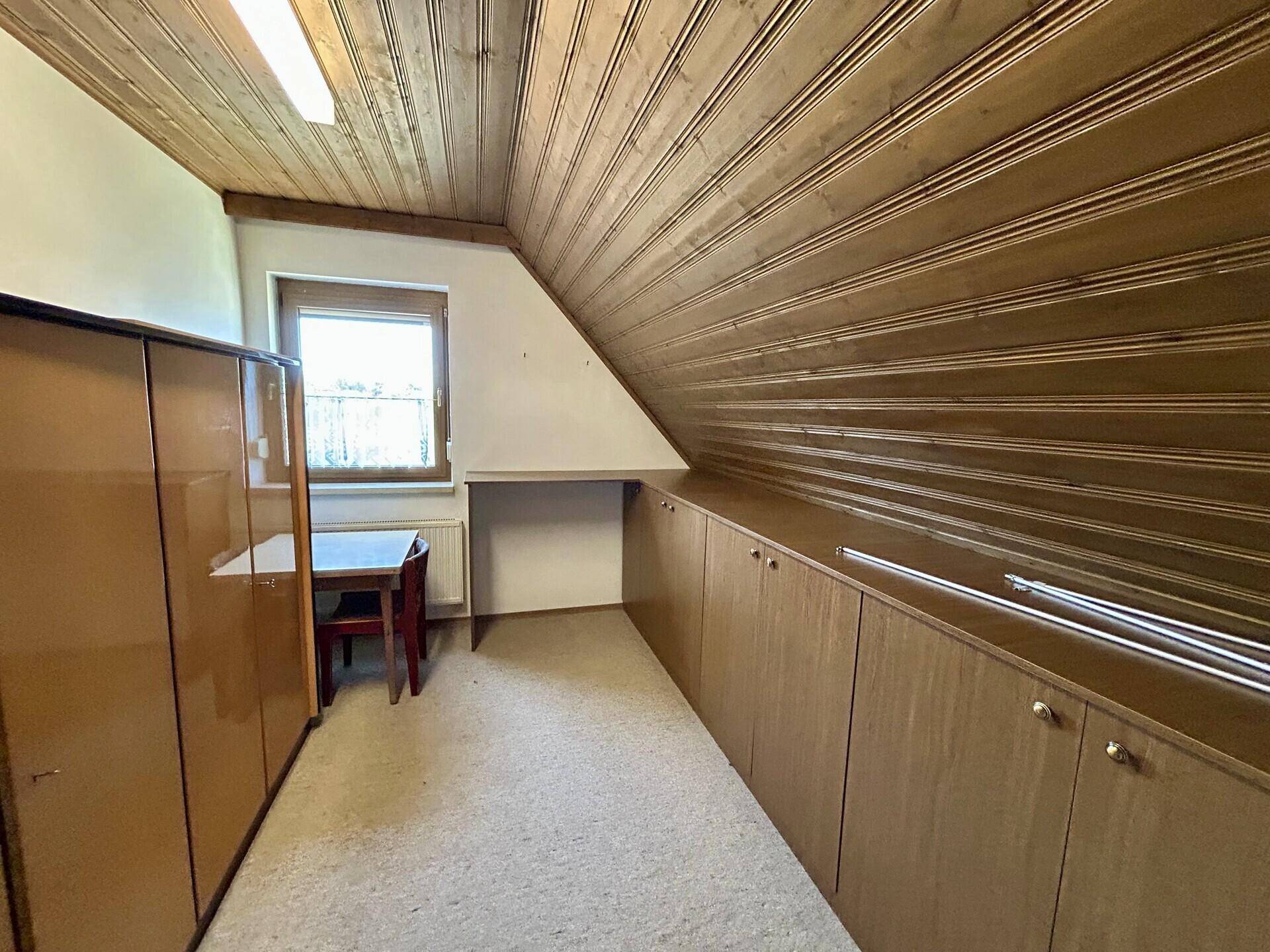 Dachgeschosszimmer mit Holzdecke, Fenster und integrierten Stauräumen.