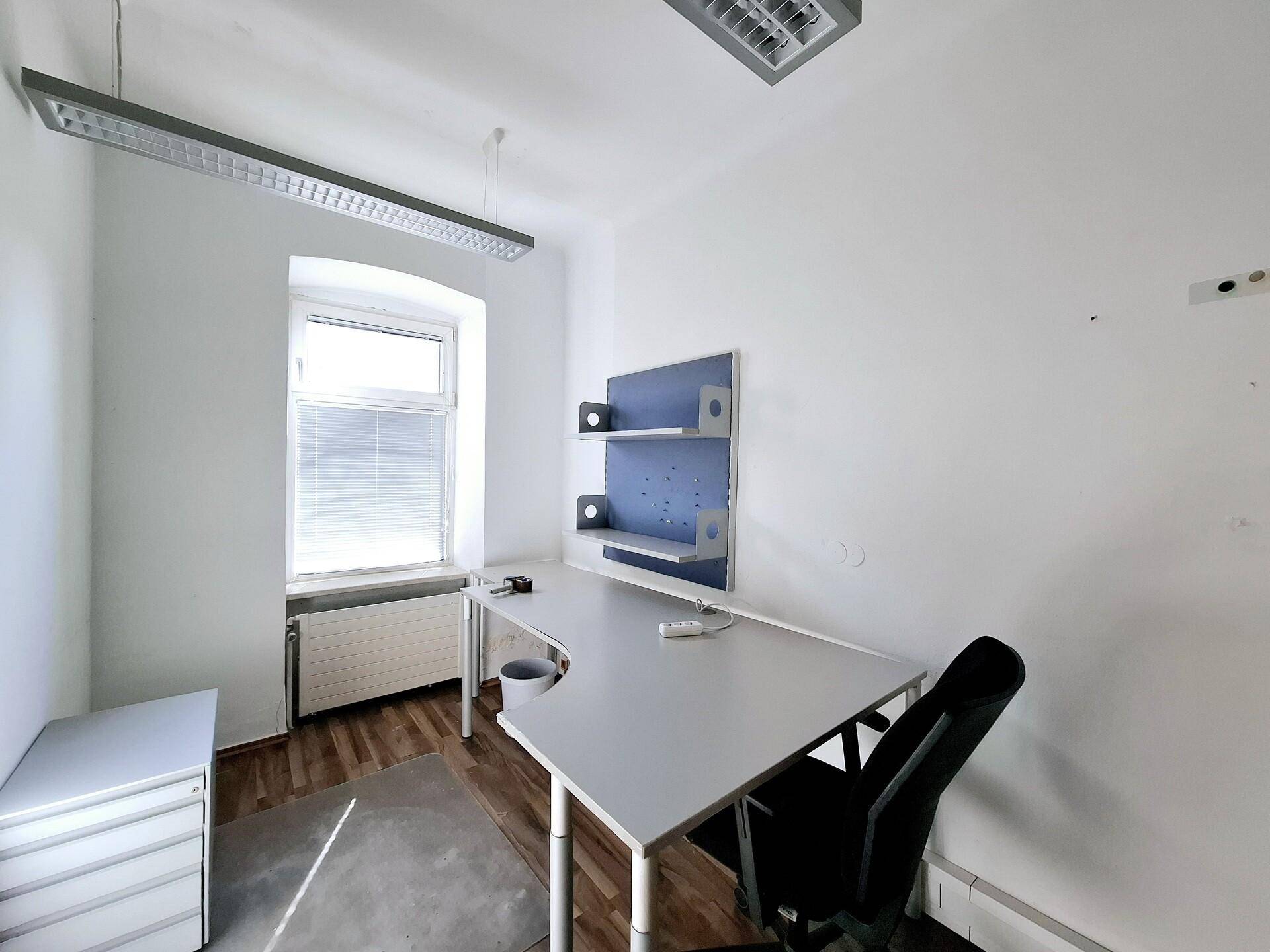 Einzelbüro mit weißer Wand, Holzboden, Schreibtisch und einem Fenster, das viel Licht hereinlässt.