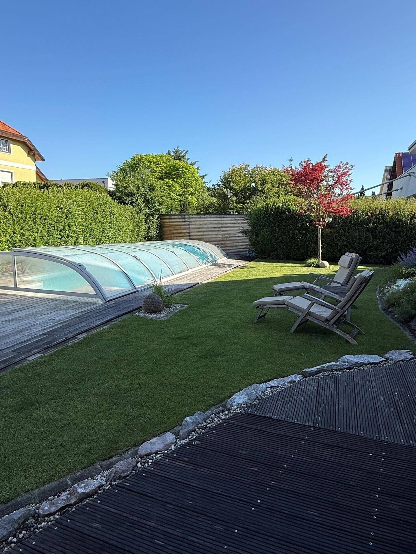 Gepflegter Garten mit Rasenfläche, überdachtem Pool und bequemen Liegestühlen für Entspannung.