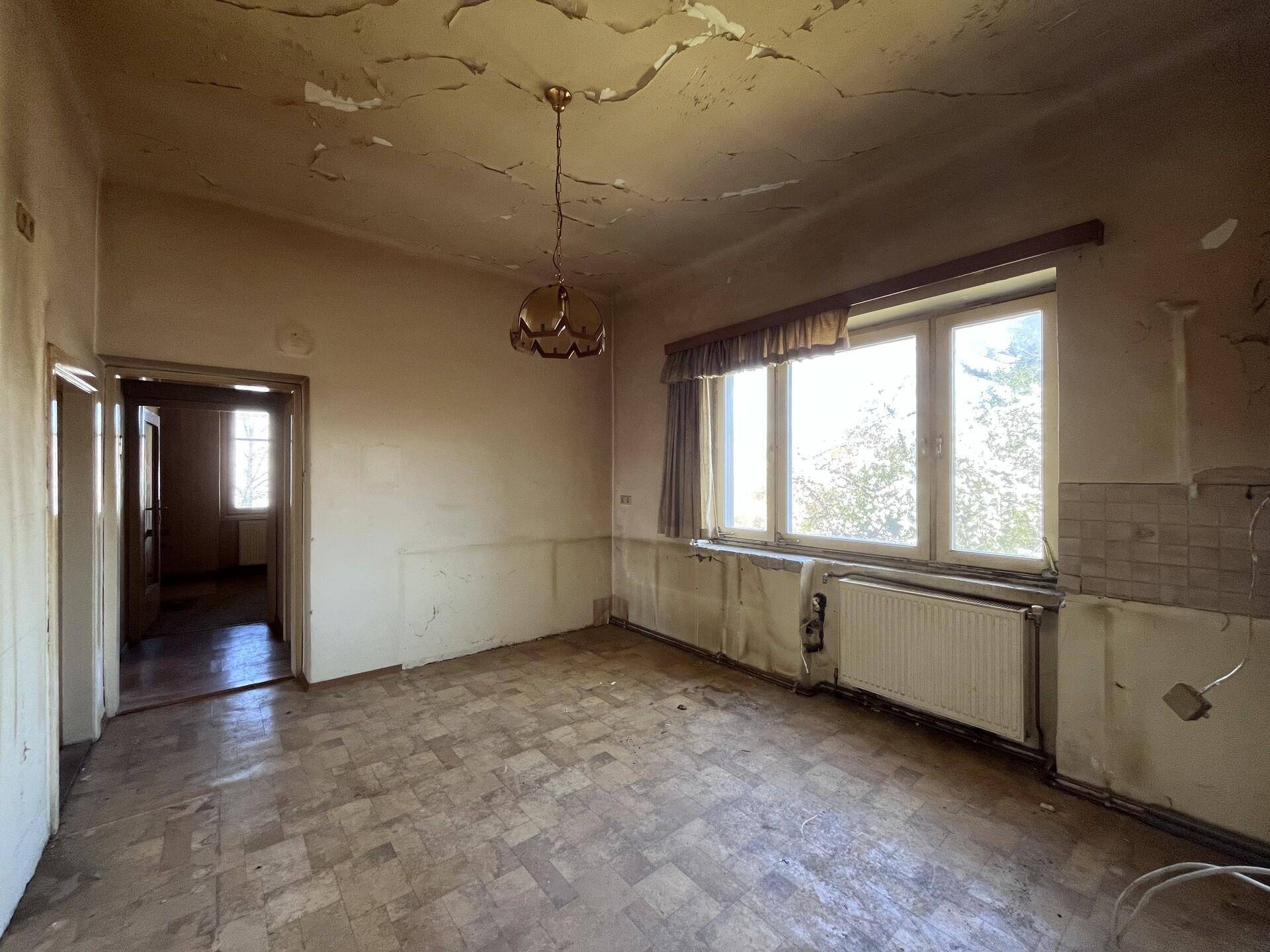 Raum mit gemustertem Boden, großen Fenstern und beschädigter Decke, renovierungsbedürftig.
