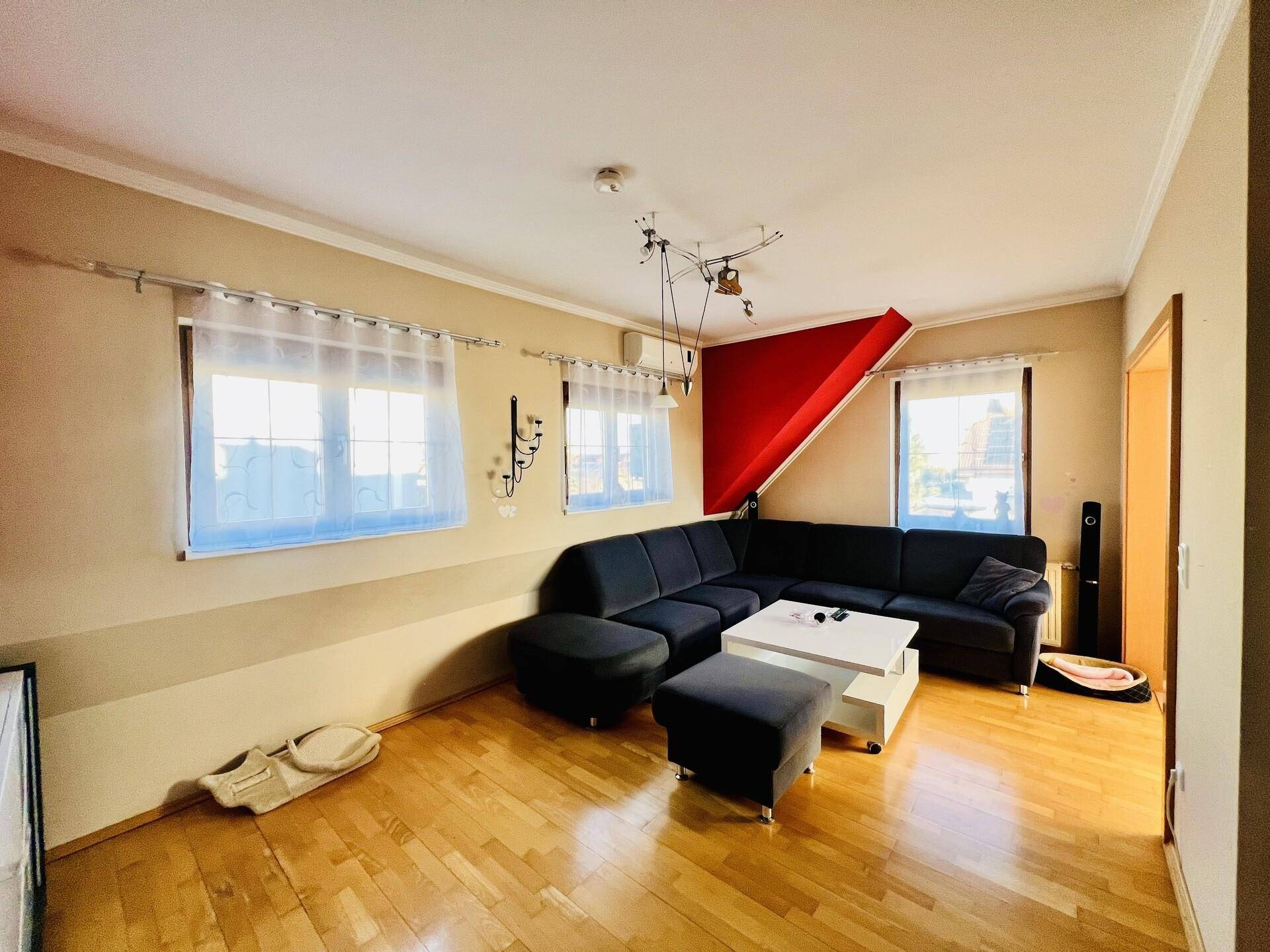 Gemütliches Wohnzimmer im Dachgeschoss mit Ecksofa, Holzboden und farbigen Wänden.