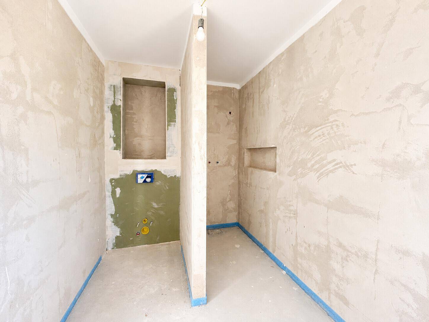 Unfertiges Badezimmer mit vorbereiteten Installationen für Dusche und WC, bereit für die Endmontage.
