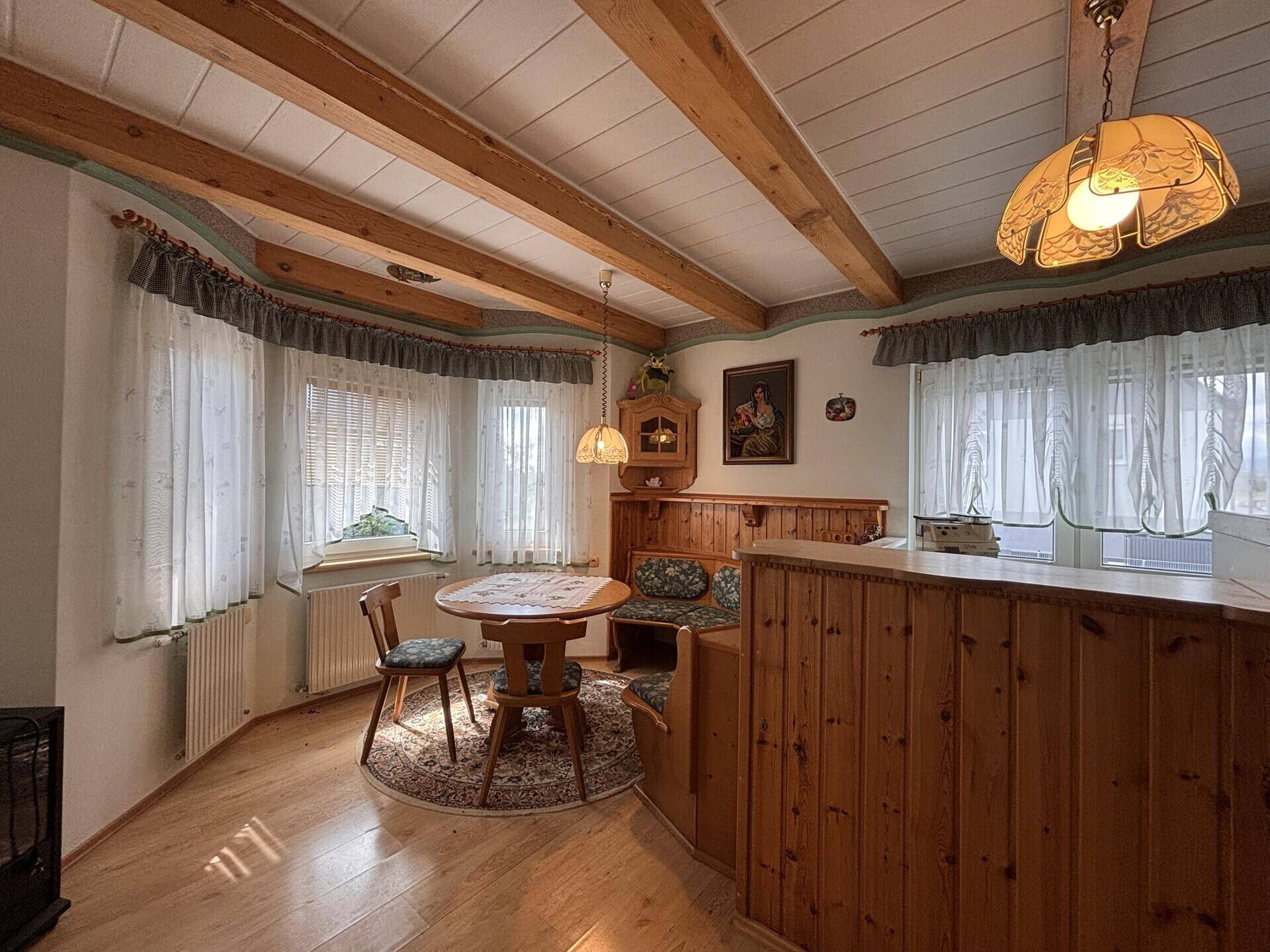 Gemütlicher Essbereich im Landhausstil mit Holzbalkendecke, Eckbank und einem runden Holztisch.