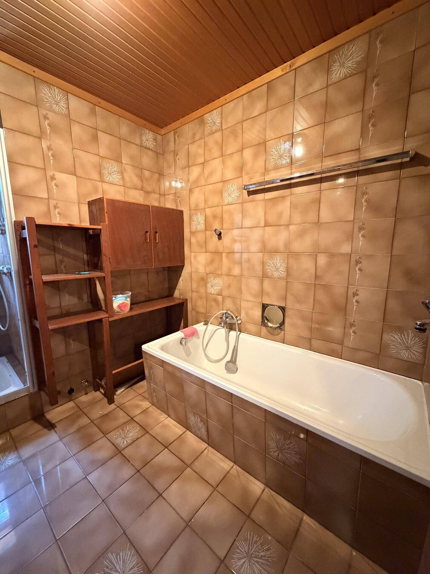 Badezimmer im 80er-Jahre-Stil mit braunen Fliesen, Badewanne und Holzdecke.