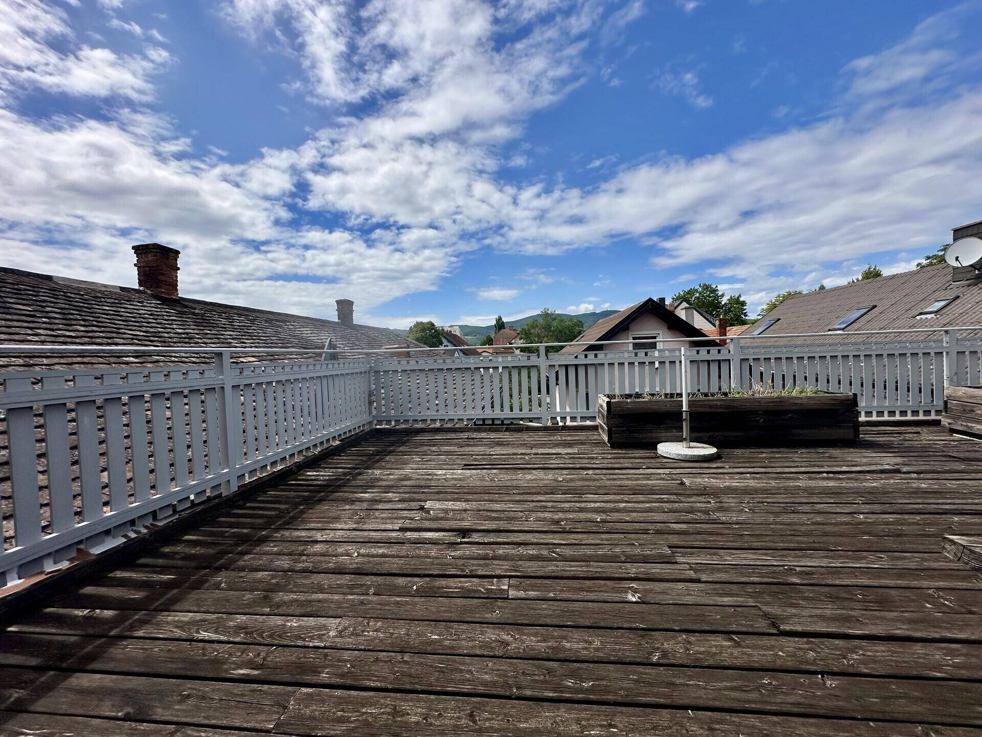 Große Dachterrasse aus Holz mit weißem Geländer und Blick auf die Umgebung.