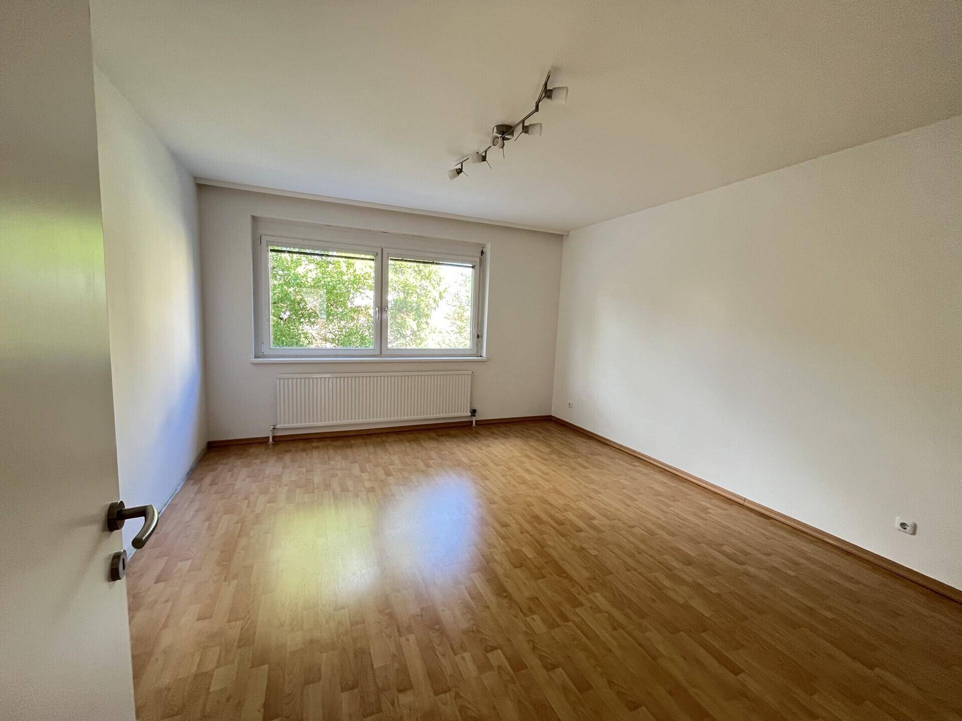Heller Raum mit Laminatboden und großem Fenster, das einen angenehmen Blick ins Grüne bietet.