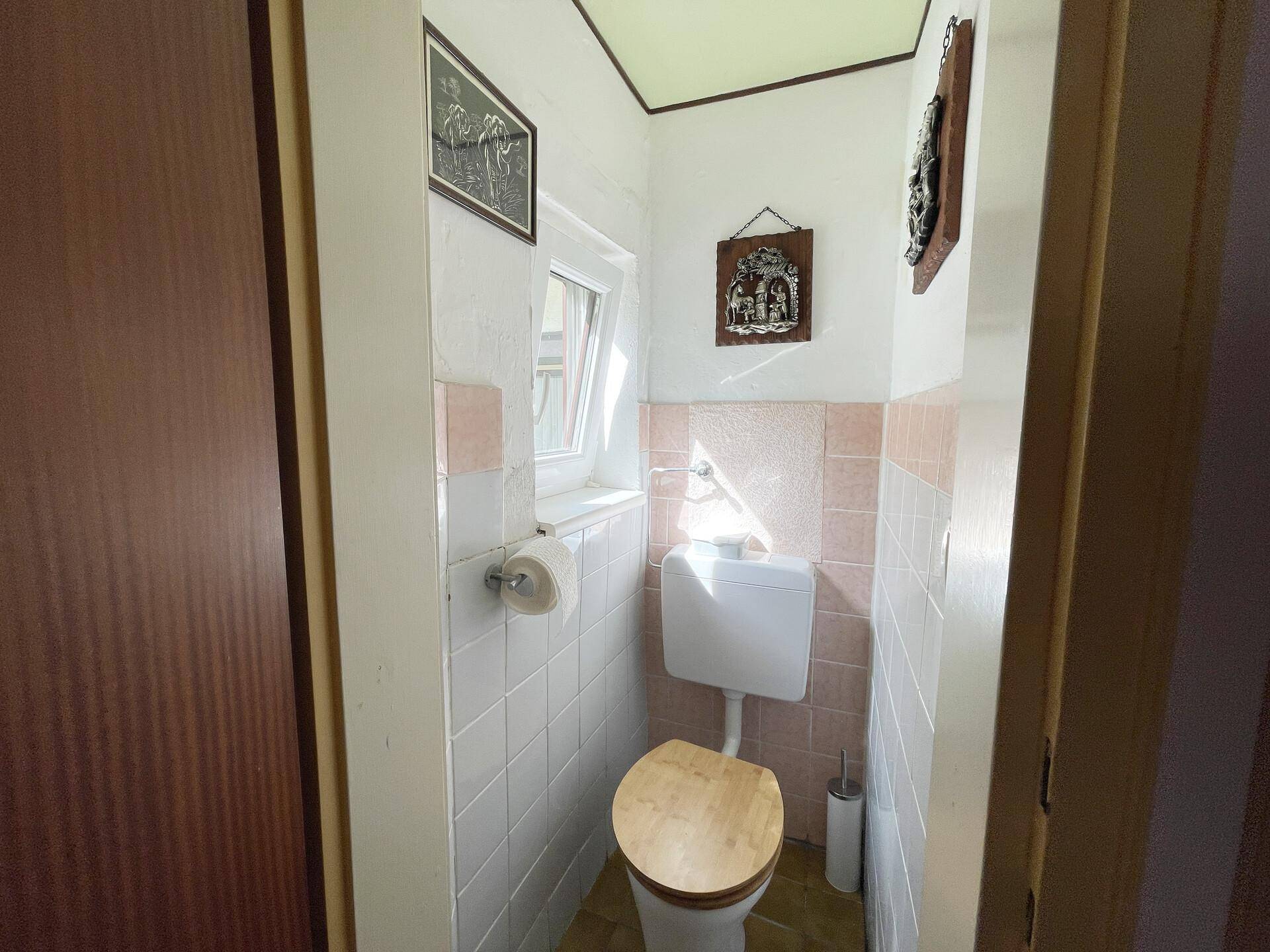 Kleines Gäste-WC mit Fenster, weißen Fliesen und Holz-Toilettensitz.