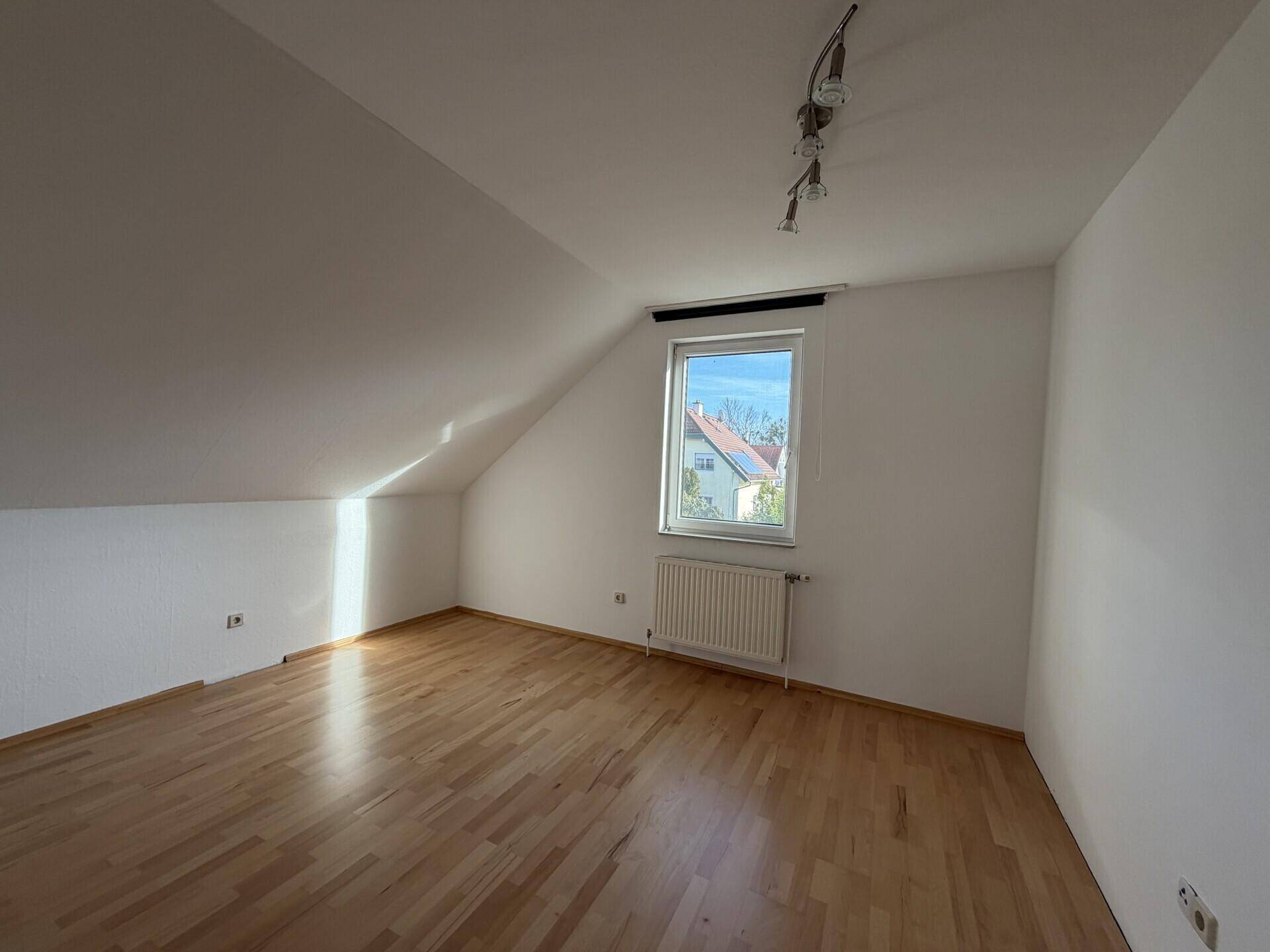 Schlafzimmer im Dachgeschoss mit Parkettboden, Dachschräge und einem Fenster für Tageslicht.