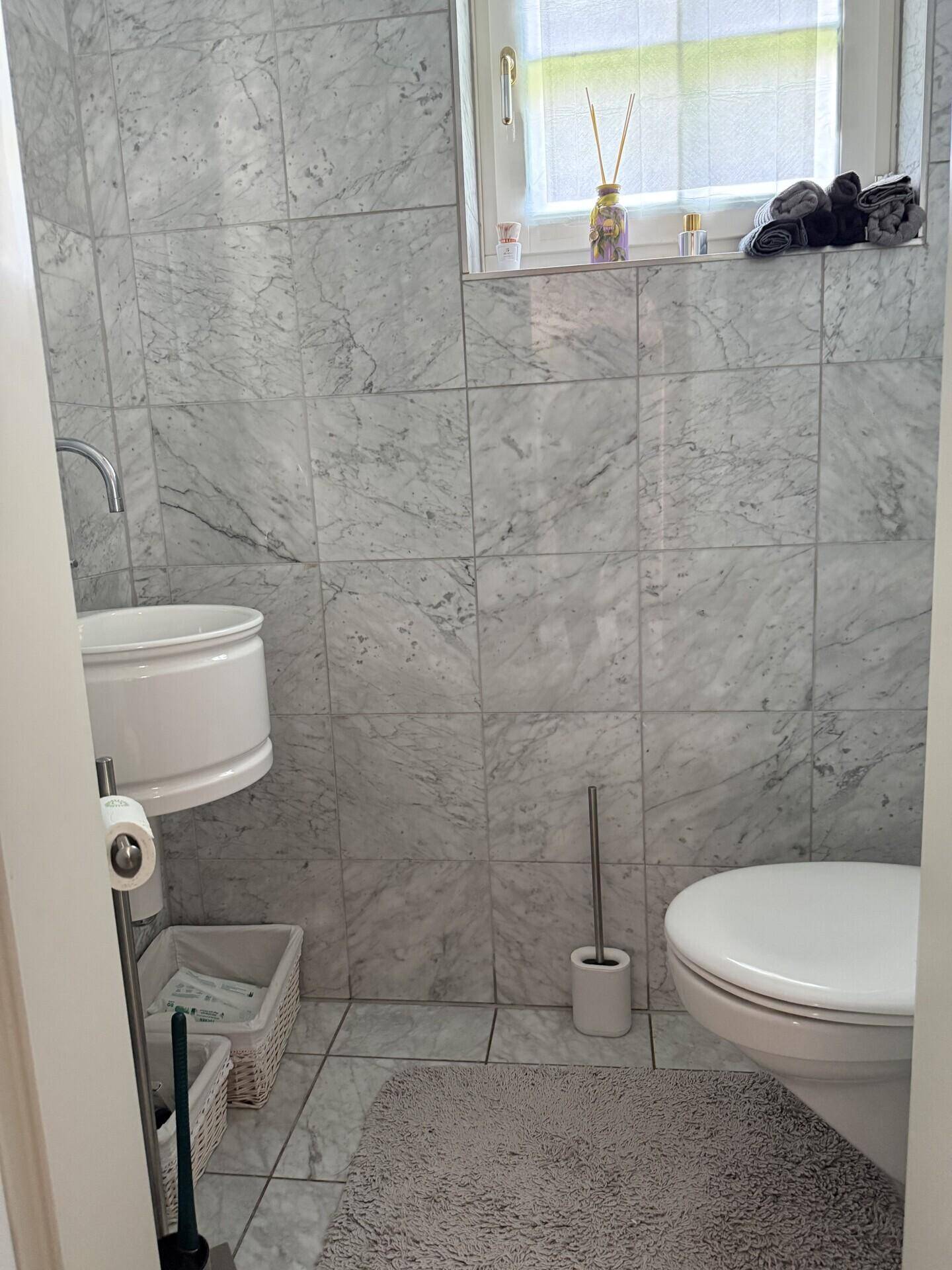 Kleines Gäste-WC mit Marmorfliesen, wandmontiertem Waschbecken und Toilette.