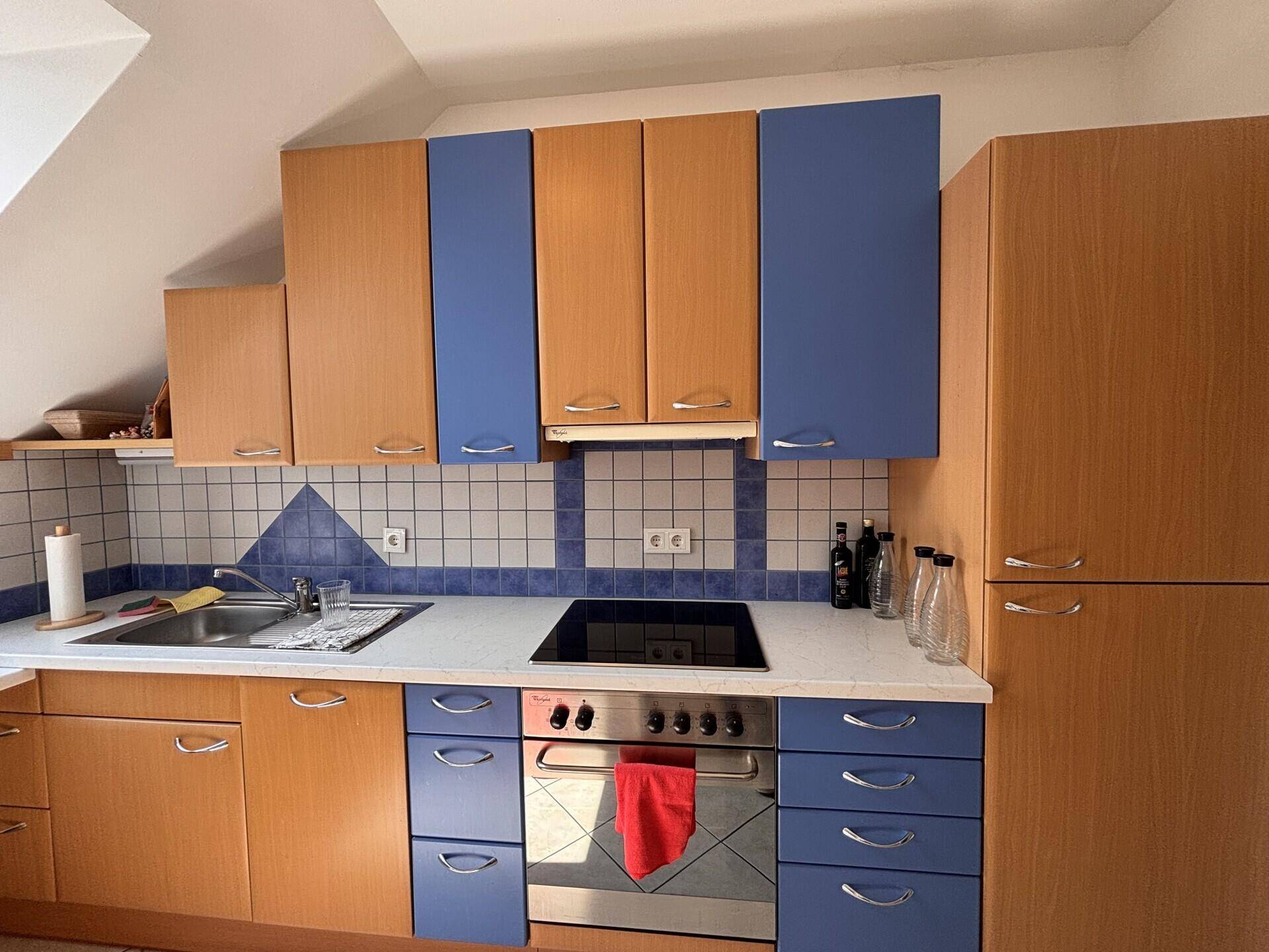 Detailansicht der Küche mit Holz- und blauen Schränken, Induktionskochfeld und Backofen.
