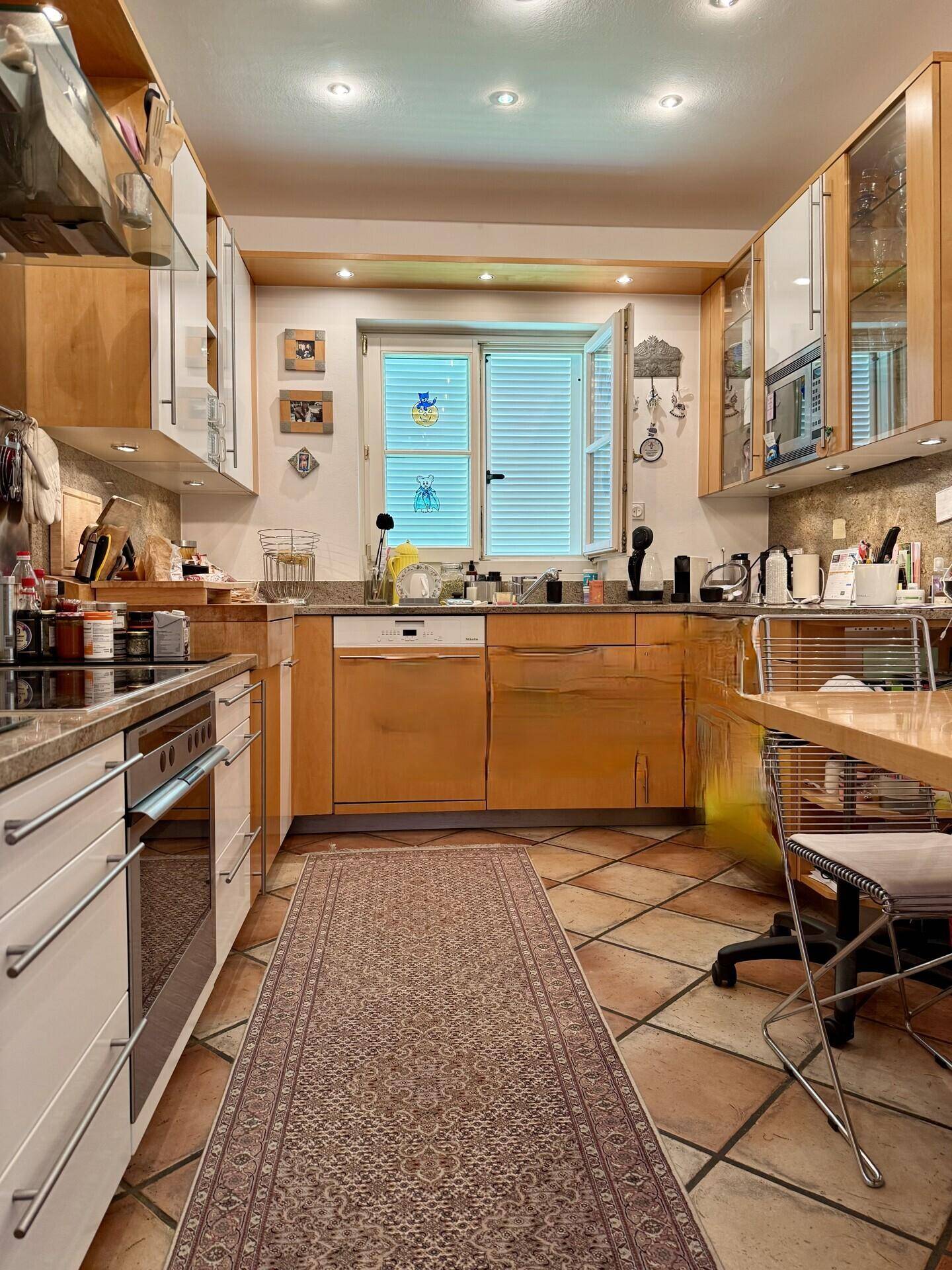 Funktionale Küche mit Holzschränken, Terrakottafliesen und Fenster über der Spüle.