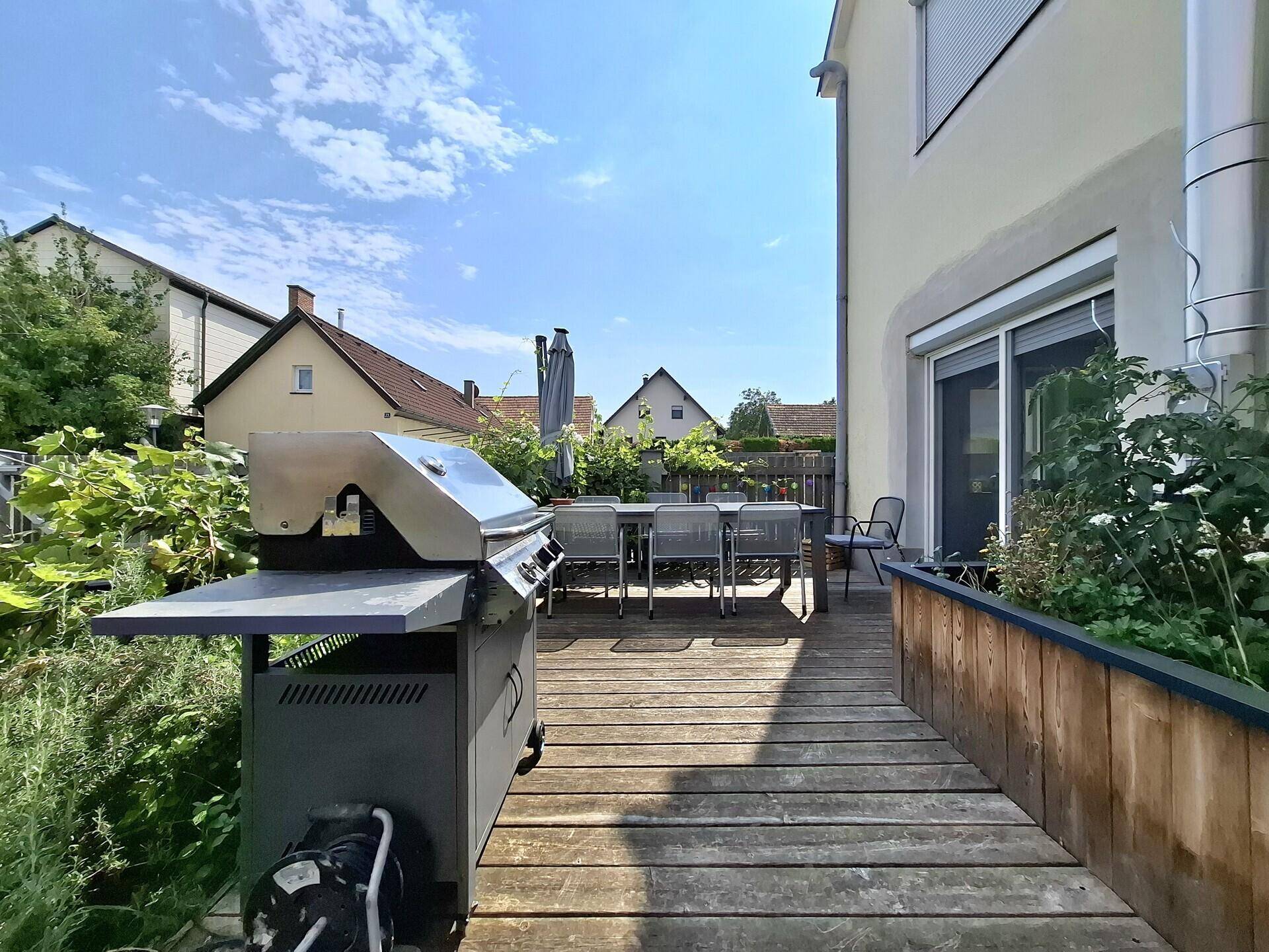 Holzterrasse mit Grillbereich und Esstisch im Freien, ideal für sommerliche Abende.