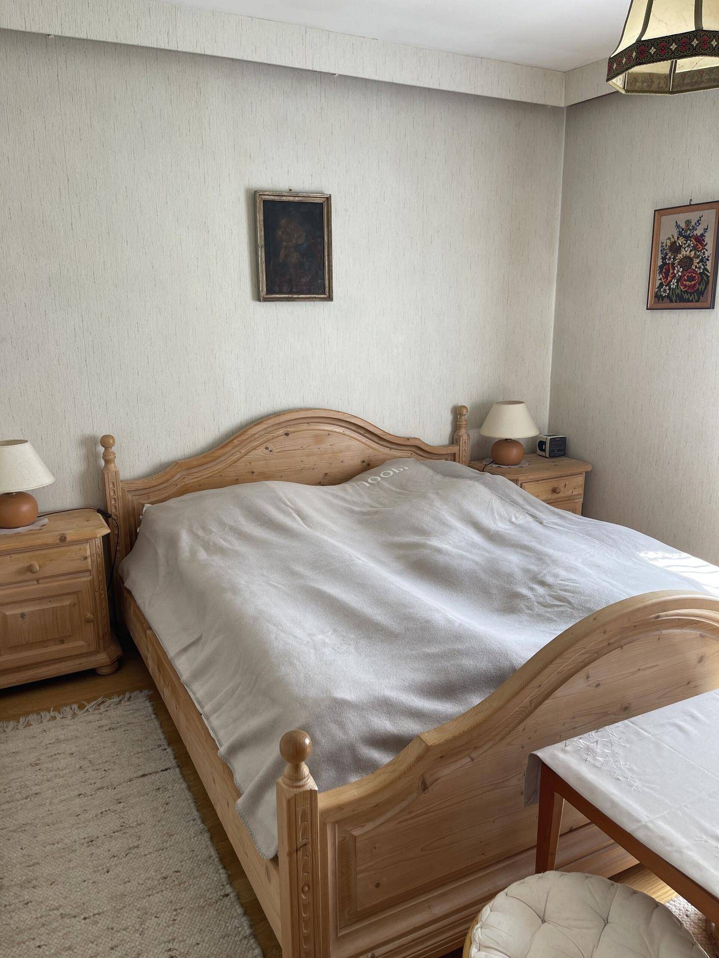 Schlafzimmer mit hellem Holzbett, Nachttischen und schlichter Tapete.