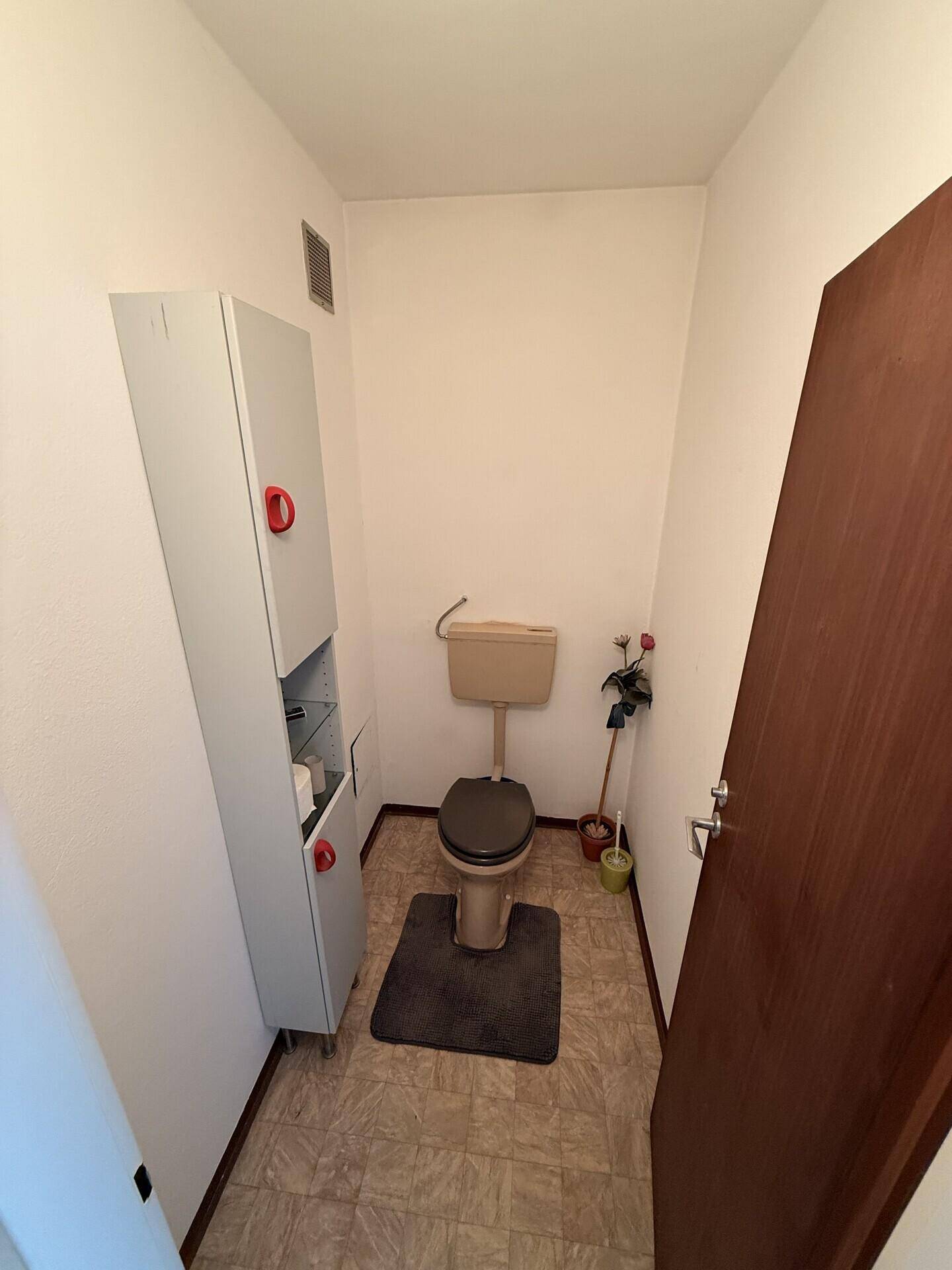 Separates Gäste-WC mit beigefarbenen Fliesen und kleinem Schrank.