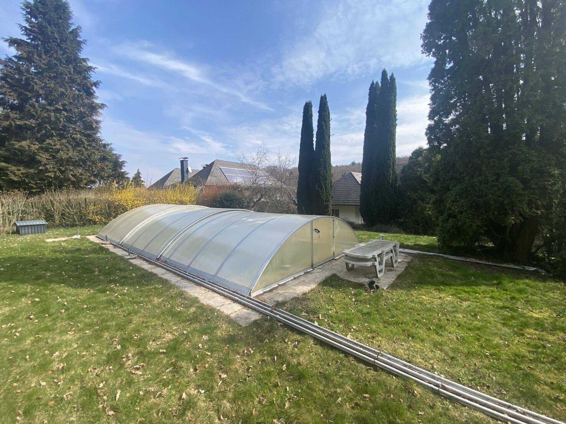Großer Garten mit Rasenfläche, hohen Bäumen und einem überdachten Swimmingpool.