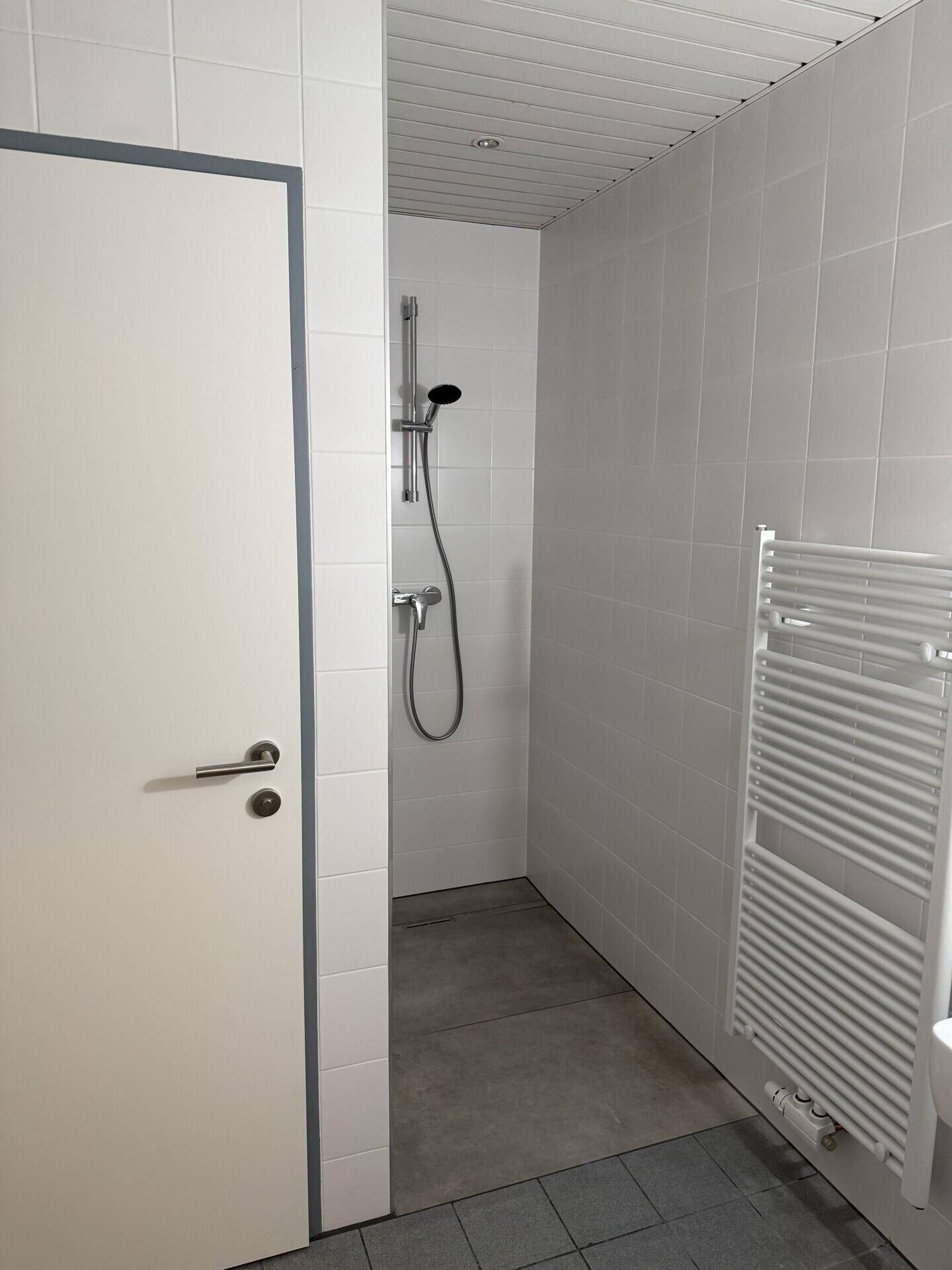 Duschbereich mit weißen Fliesen und einem modernen Handtuchheizkörper an der Wand.