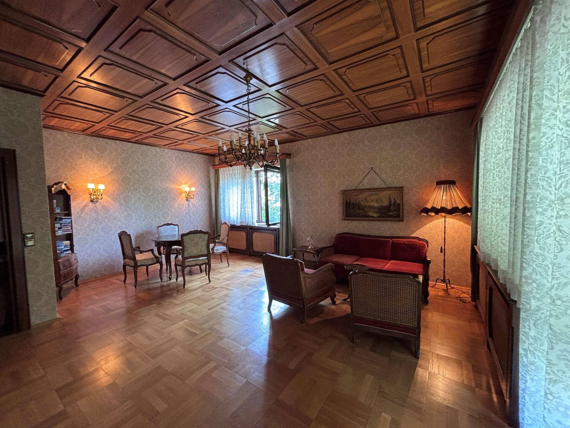 Geräumiges Wohnzimmer mit Holzkassettendecke, Parkettboden und traditionellen Möbeln.