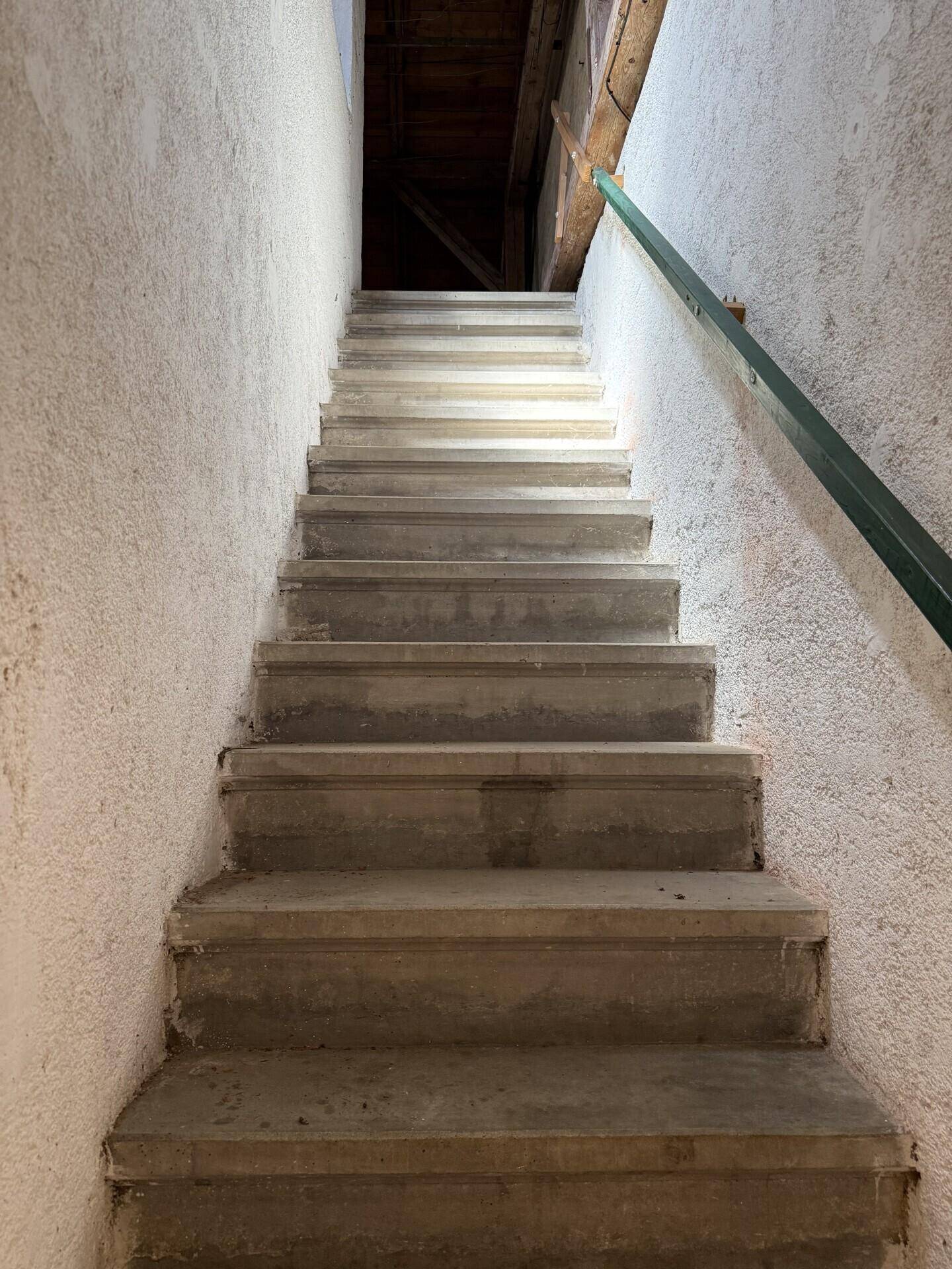 Betontreppe mit grünem Handlauf führt in den oberen Bereich des Hauses.