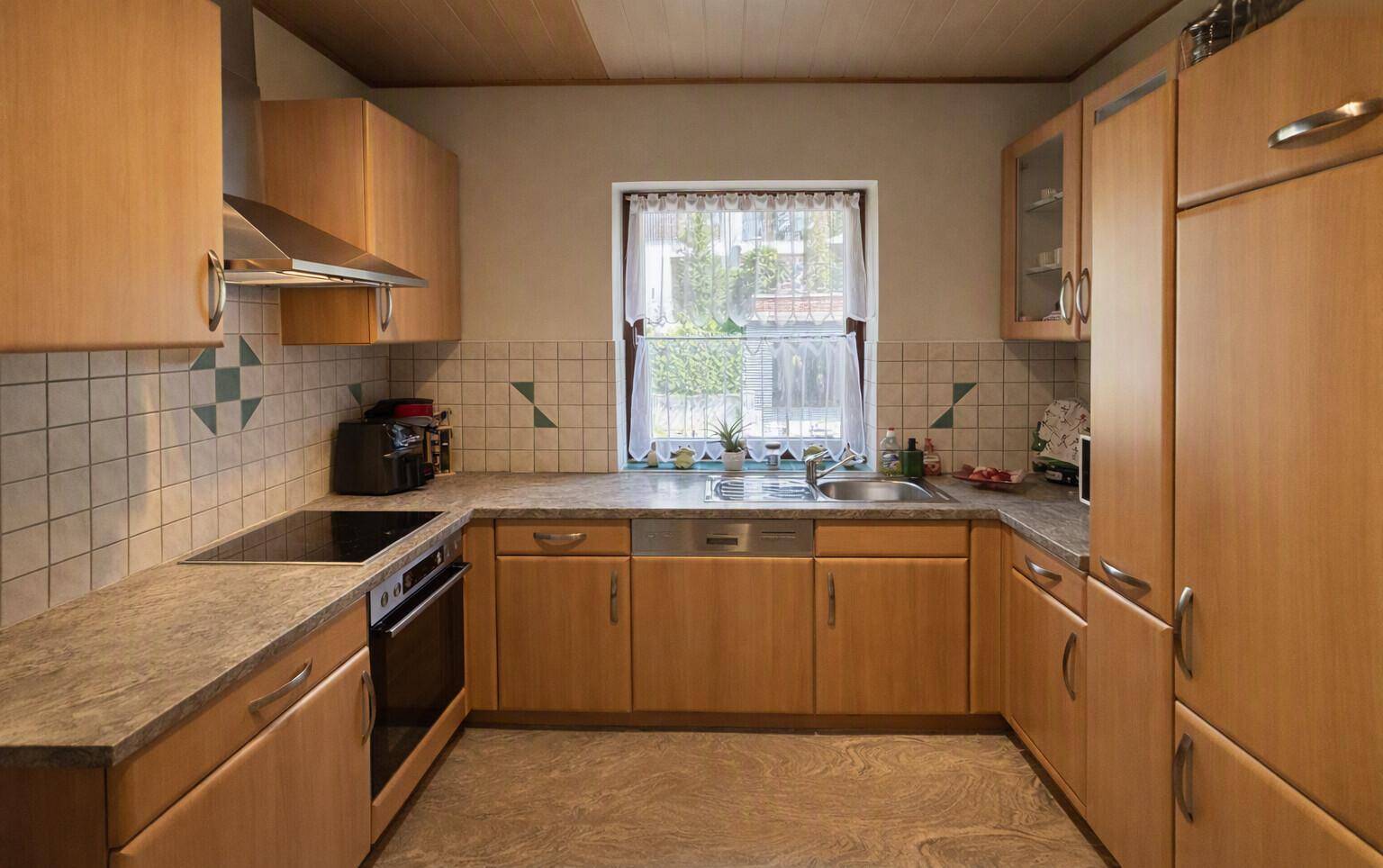 Funktionale Küche mit Holzschränken, hellen Fliesen und einem Fenster über der Spüle.