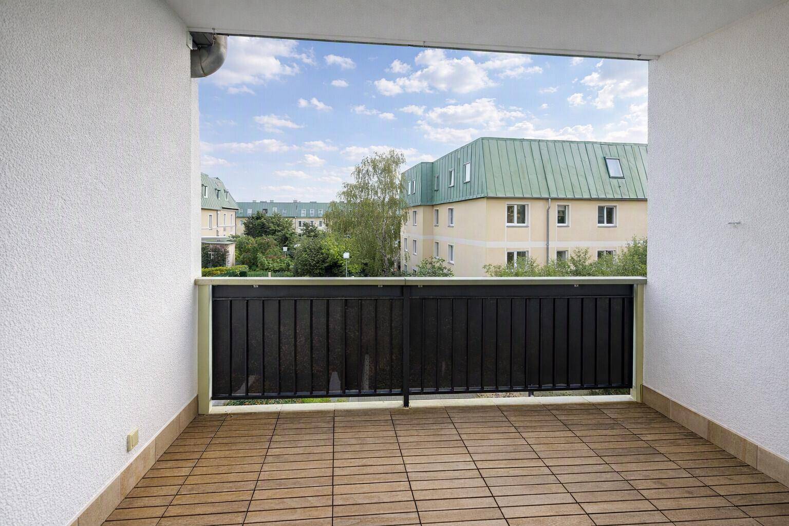 Überdachter Balkon mit Holzboden und Blick auf die umliegenden Gebäude und Grünflächen.