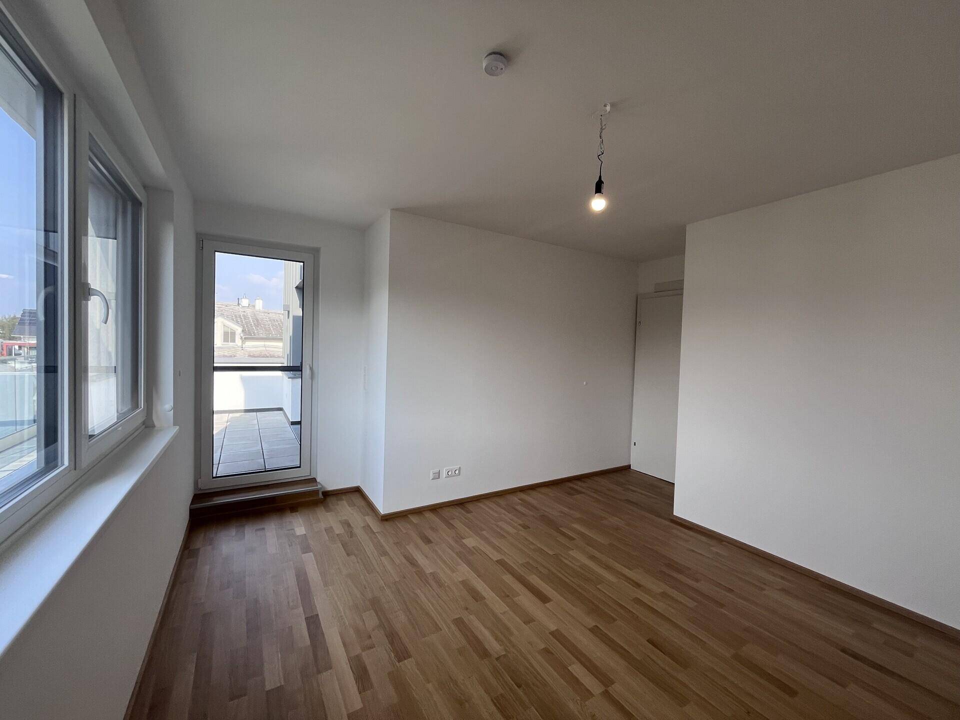 Schlafzimmer mit Parkettboden und großen Fenstern, die viel Tageslicht hereinlassen.