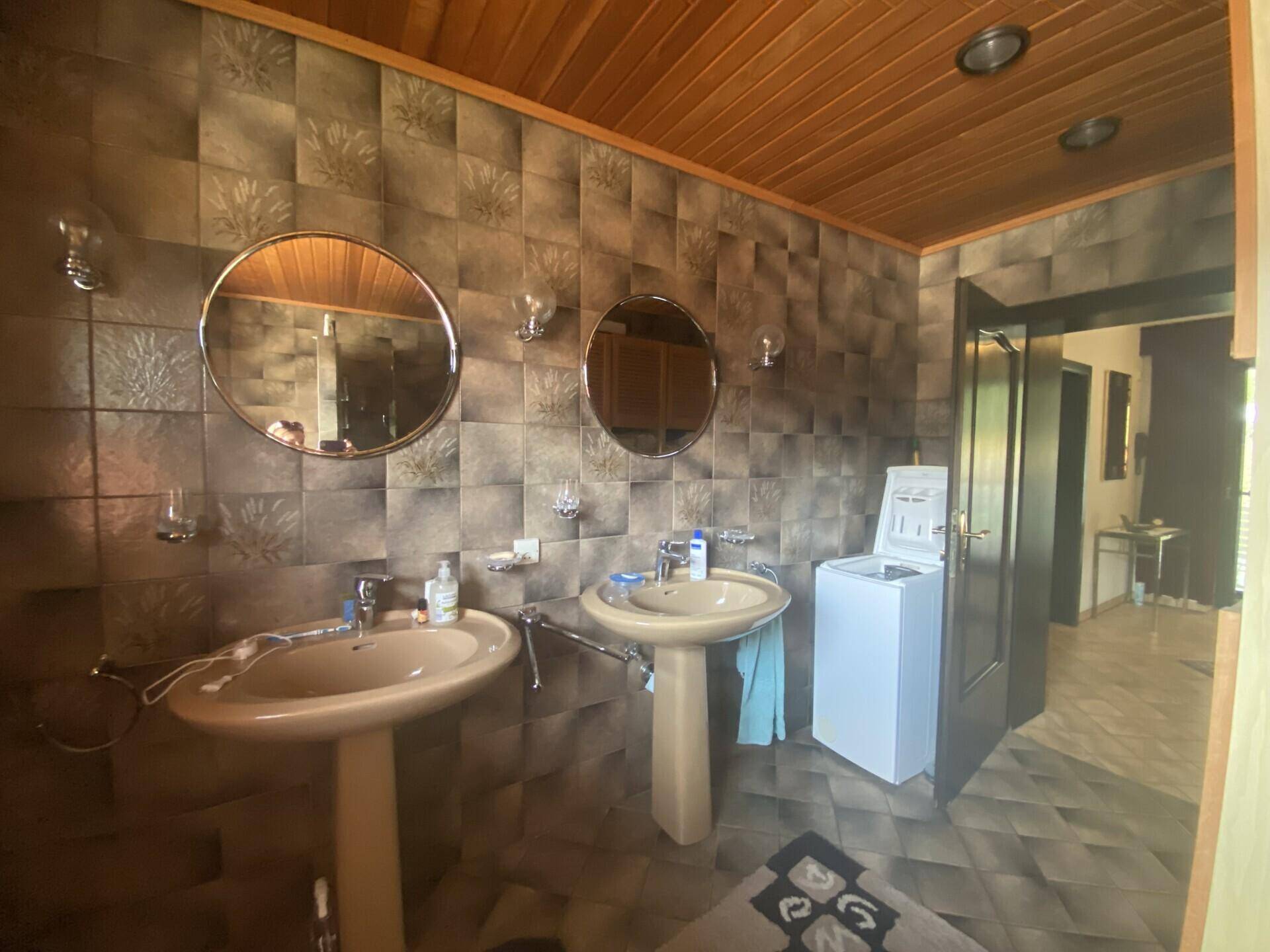 Badezimmer mit zwei Waschbecken, gemusterten Fliesen und Holzdecke, inklusive Waschmaschine.