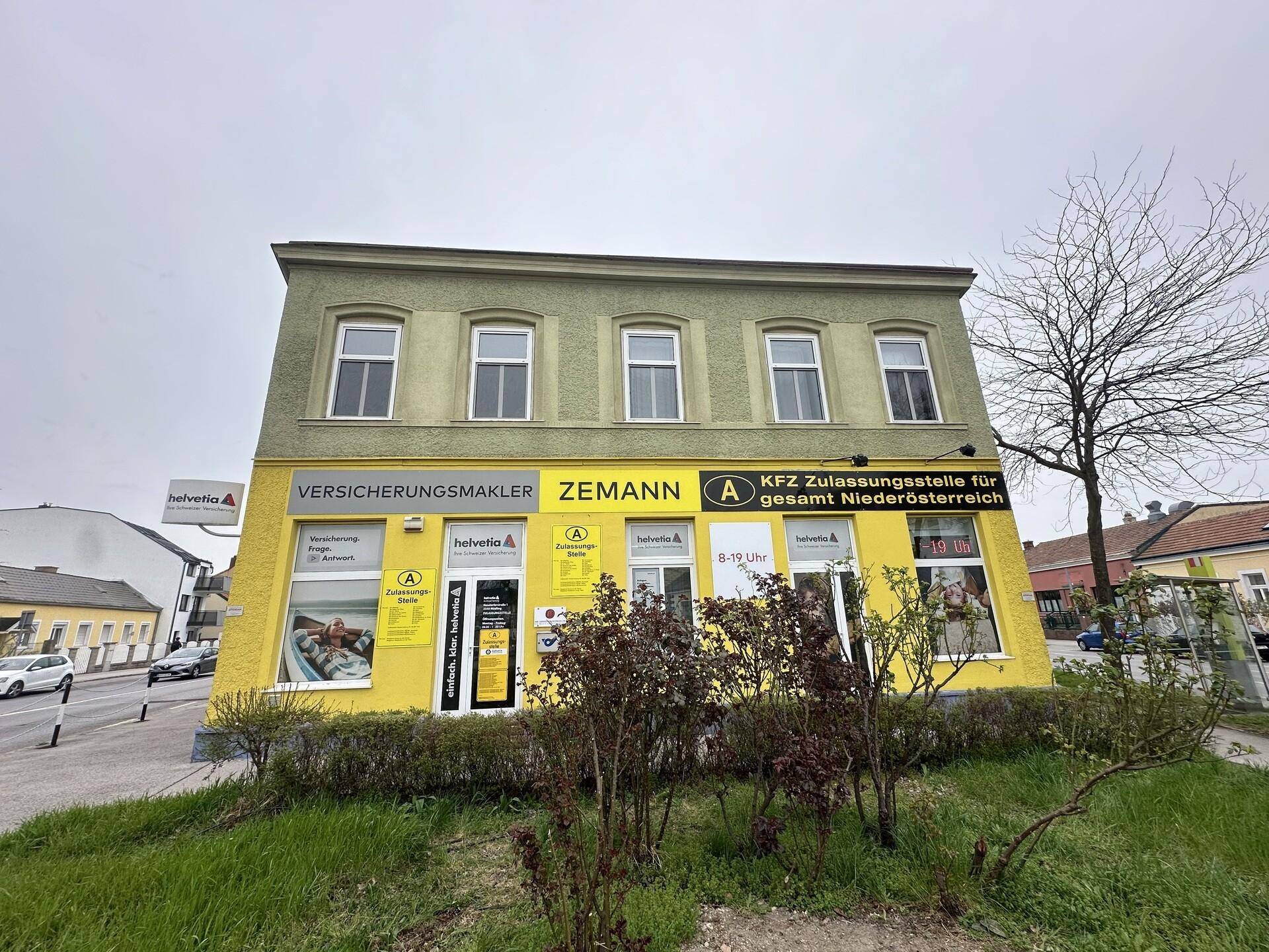 Vorderansicht des Gebäudes mit gelben Geschäftsflächen im Erdgeschoss und grüner Fassade.